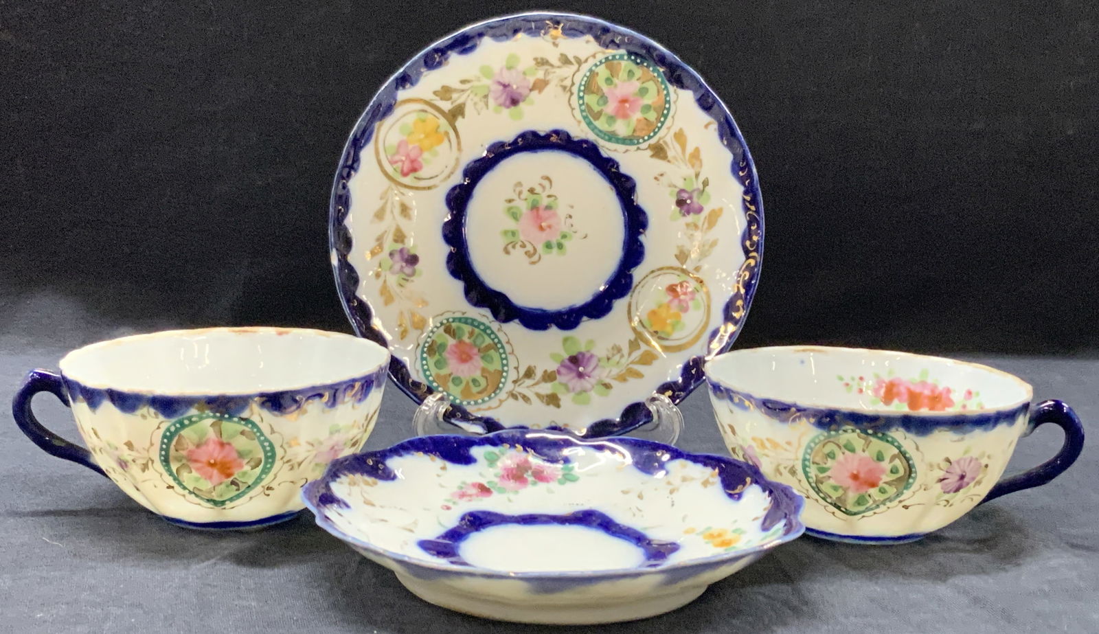 Lot 4 Hand Painted Gilt Bone China Cups & Saucers: Lot of 4 pieces of bone China. 2 hand painted tea cups with blue bands and hand painted flowers amongst gilt outlines and scroll designs. 1 saucer at 5.25 inches and 1 dish with hand painted floral mo