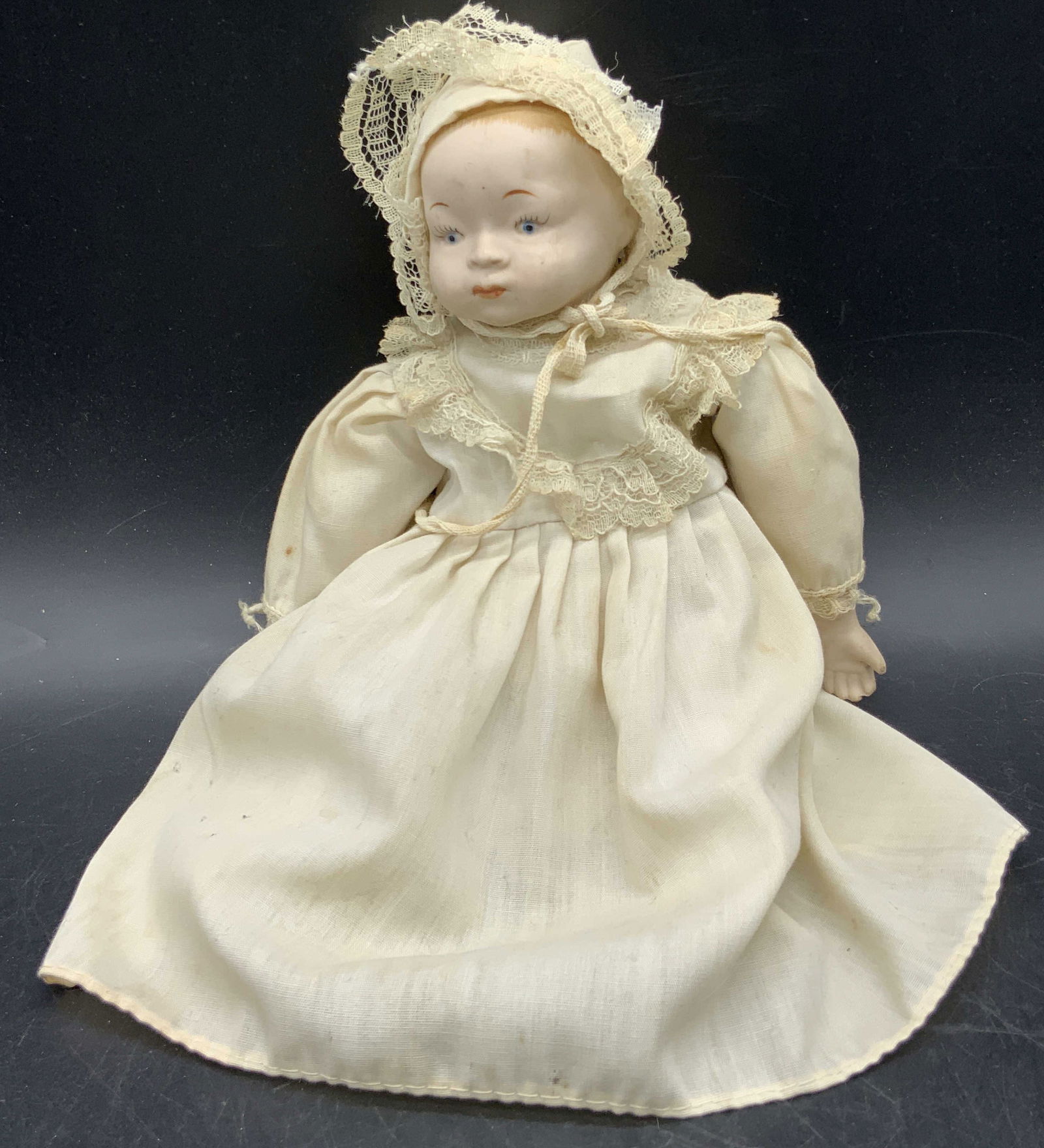Vintage Porcelain Doll W/ Fabric Dress: A vintage porcelain limb doll with a stuffed fabric torso and a fabric dress. Measures approx. 9L x 4W in. Measured at widest point. Some losses to the fabric present. Some discoloration and surface w