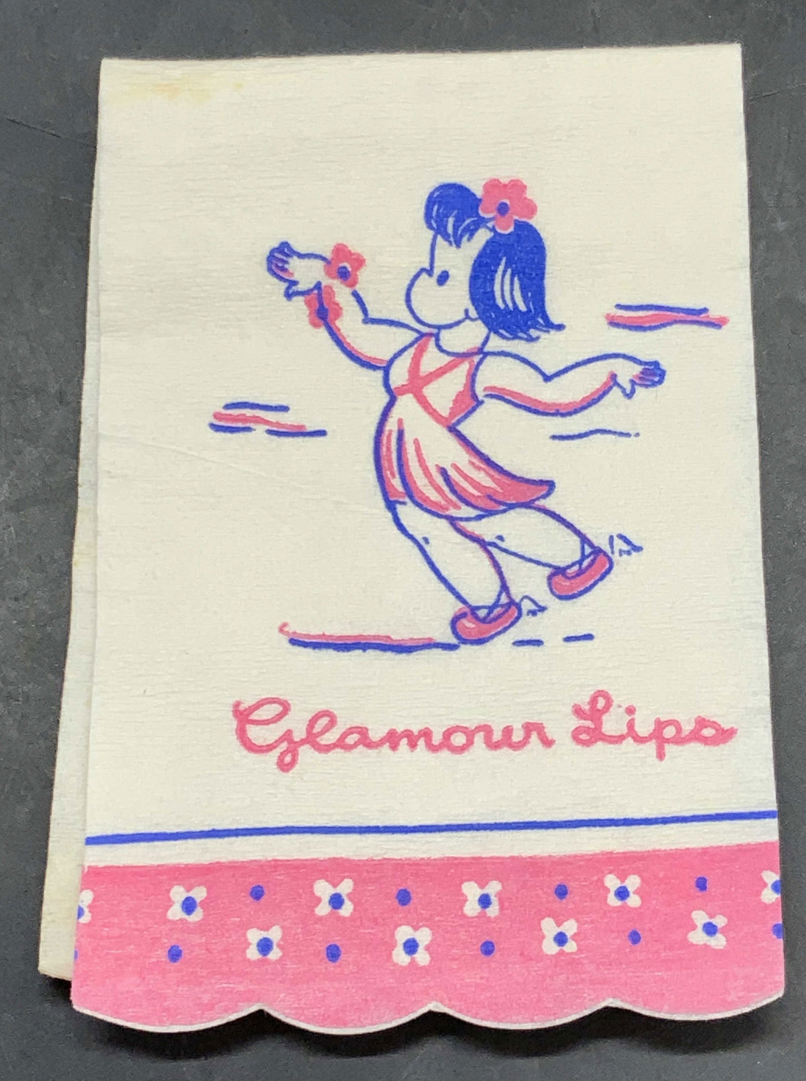 GLAMOUR LIPS Vintage Paper Napkin Ephemera: A vintage paper napkin that features a dancing girl to the obverse. Reads GLAMOUR LIPS beneath the dancing figure. Primarily white, pink, and blue hues. Open the piece measures approx. 7.5L x 2.5W in.