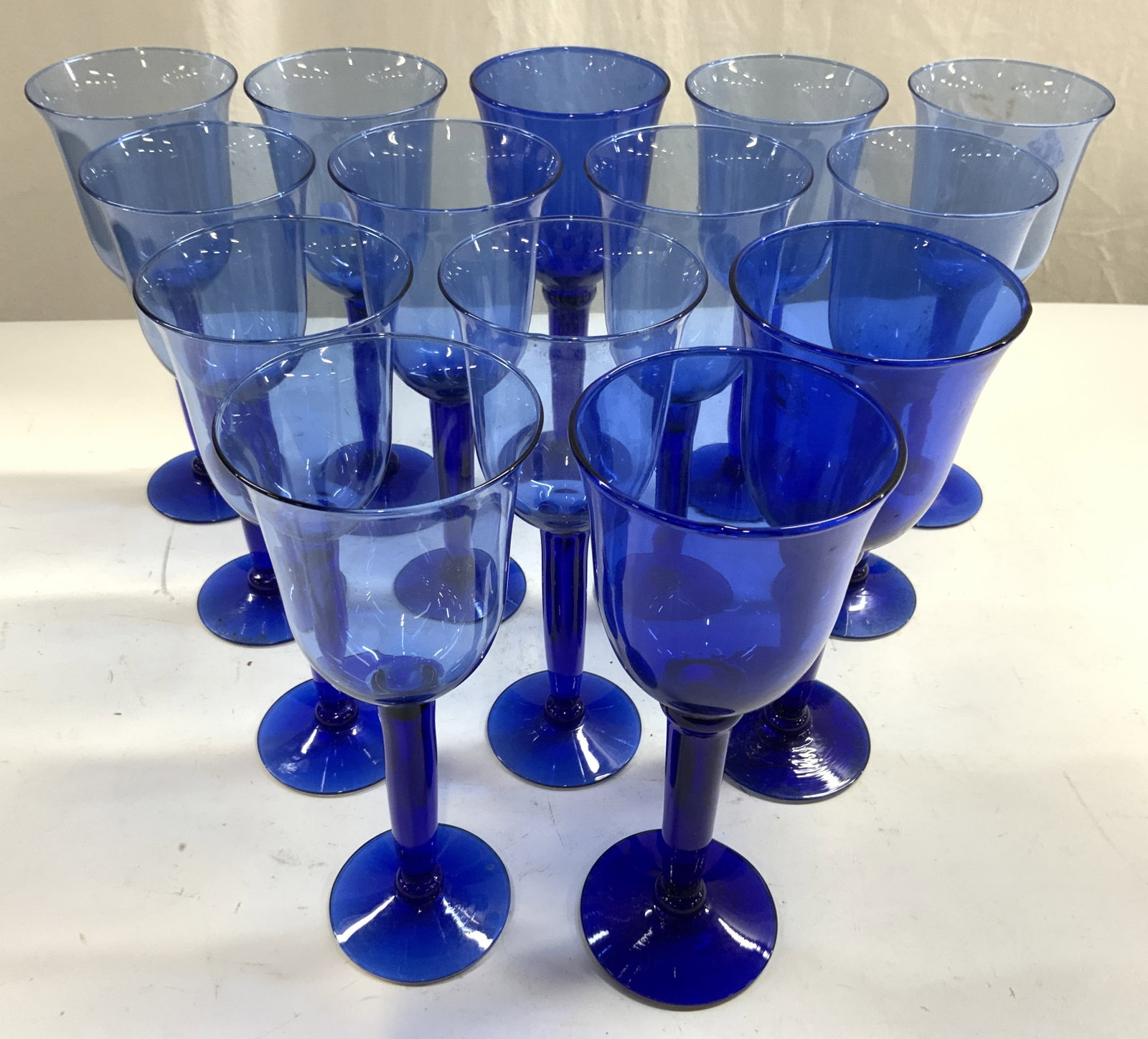 Set 14 Hand Blown Art Glass Wine Glasses Blue: One glass has tag which reads HAND BLOWN MADE IN MEXICO. Lot includes 14 wine glasses. Each piece is blue toned. Vessels each have circular form base. Three glasses are darker toned than others. Each 