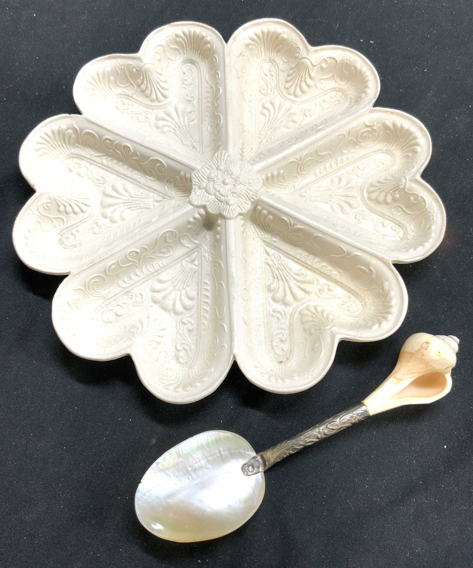 Lot 2 Ceramic Hors Doeuvres Dish & Shell Spoon: Lot includes 1 cream toned floral form hors Doeuvres dish with beveled scroll and vine detail, & 1 shell & silver plate spoon. Hors Doeuvres dish is ceramic measures approximately 8 inches wide. Hors 