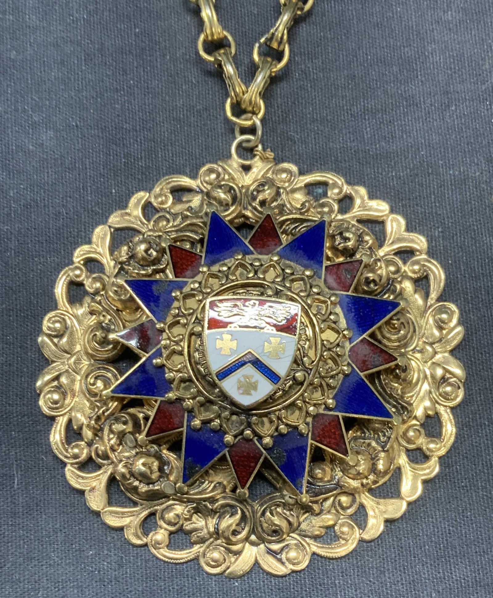 Vintage Gold Tone Crest Pendant Necklace: Vintage gold tone pendant necklace. Enameled crest motif and raised scroll detail on pendant. Drop length approx. 9 inches. Pendant measures approx. 3 inches wide. Some surface wear including scratchi