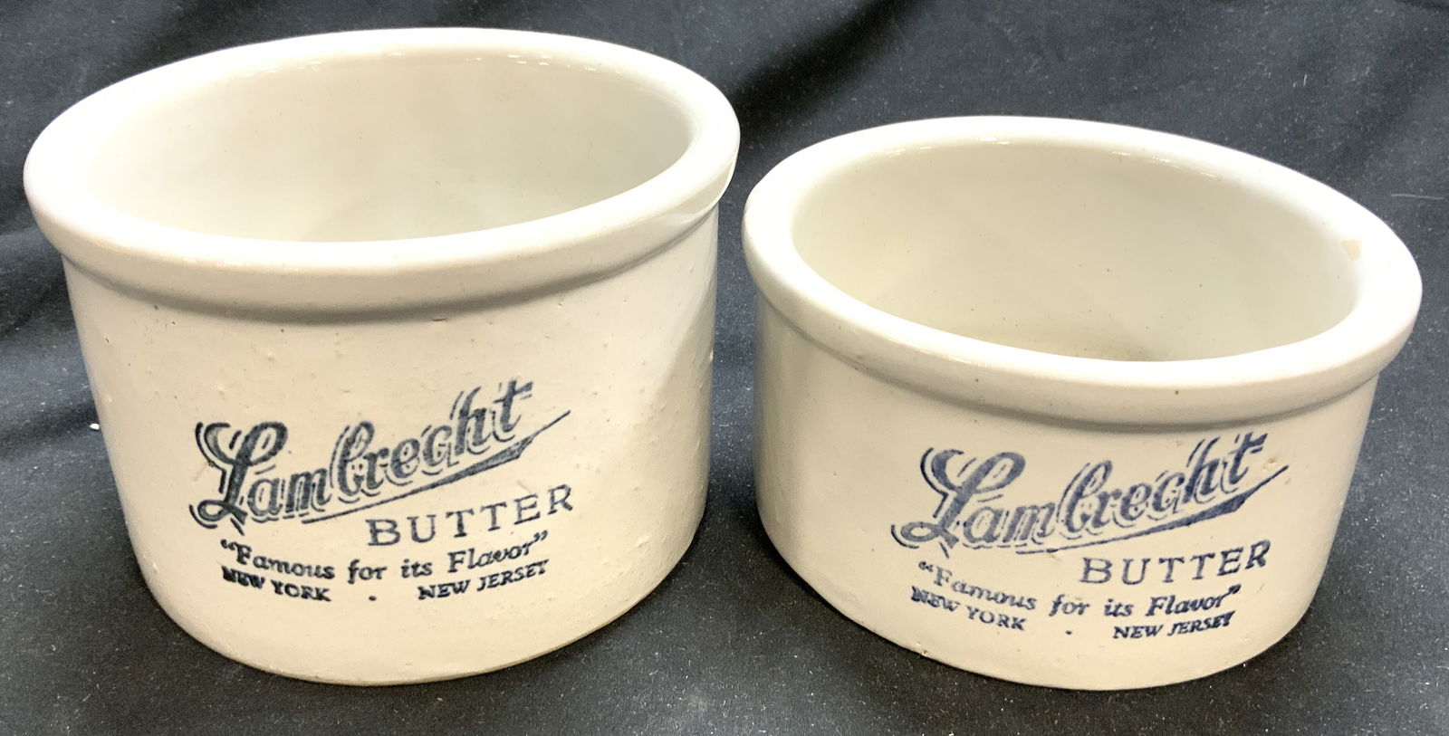 LAMBRECHT Lot 2 Stoneware Butter Crock: Each crock is marked LAMBRECHT BUTTER. Each piece is slate toned stoneware ceramic with blue toned lettering. Each piece has lipped rim. Crocks are each circular shaped. Largest piece measures approxi