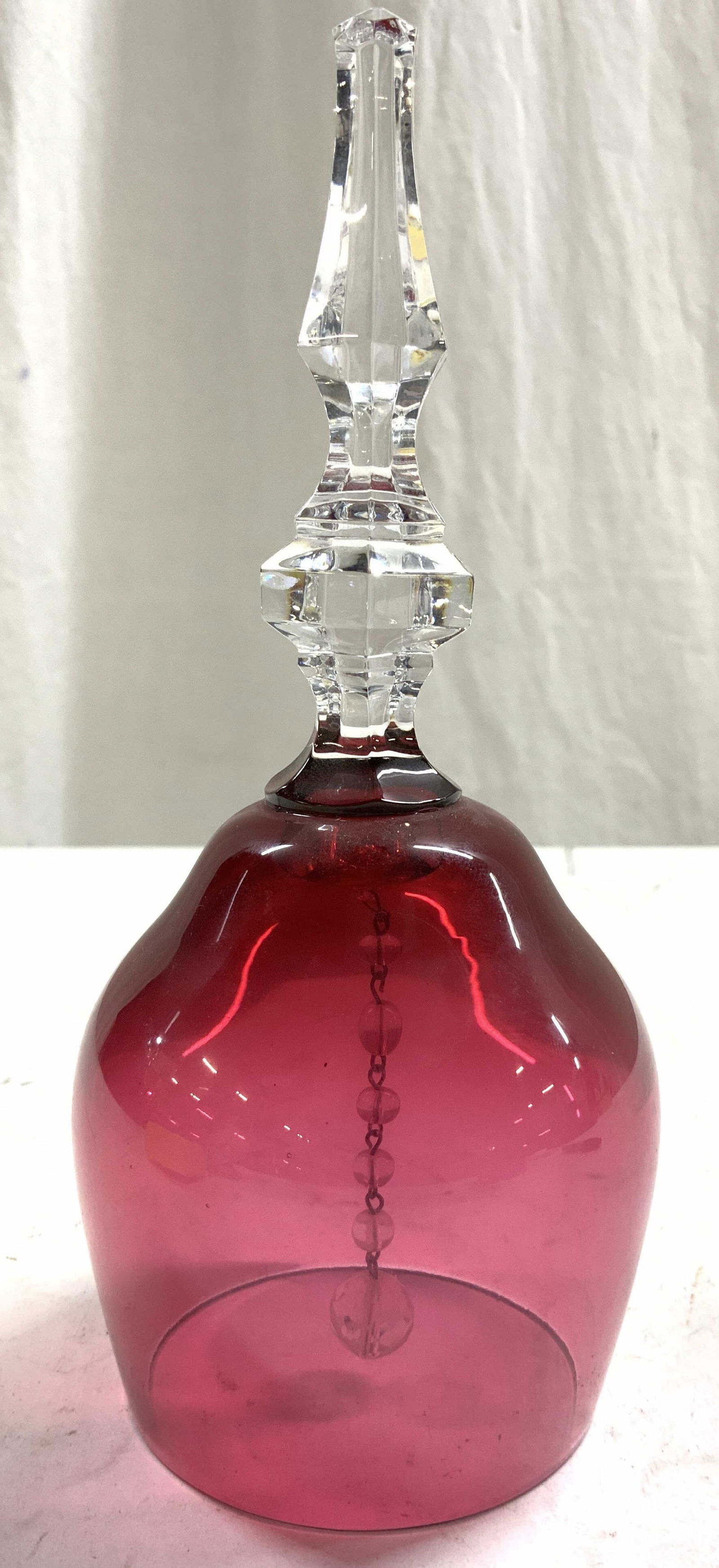 Vntg Cranberry Glass Art Glass Bell: Bell has beaded clapper inside. Piece has clear geometric handle and cranberry toned bell walls. Bell appears to be vintage. Bell measures approximately 7 inches tall 3 inches wide. Bell, glass bell,