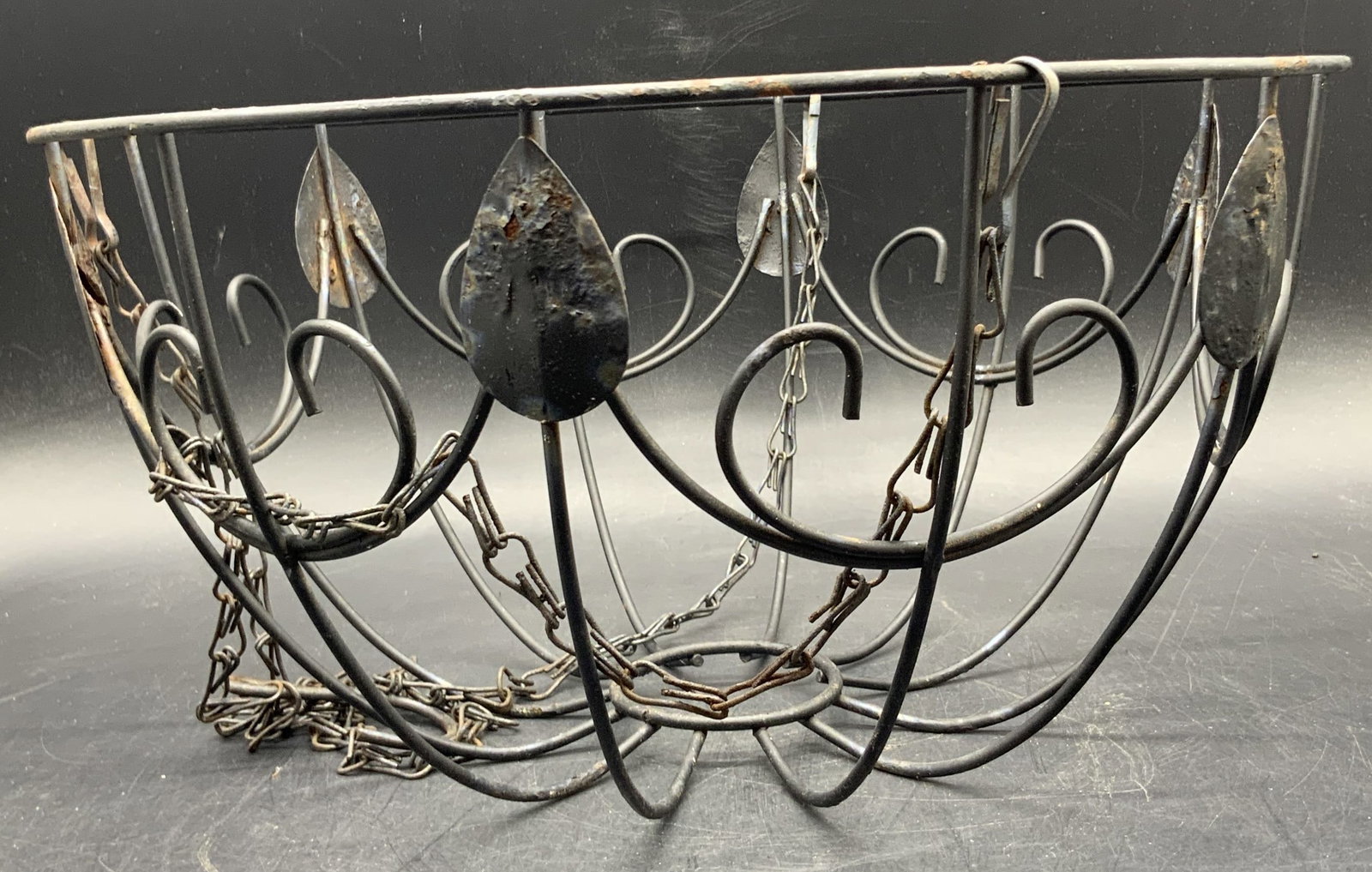 Vintage Black Metal Foliage Motif Hanging Basket: A vintage black metal foliage motif hanging basket. Basket measures approx. 6.5H x 11.5W in. Discoloration and surface wear present. Chain needs adjustment. Collectibles, garden decor, garden accents,