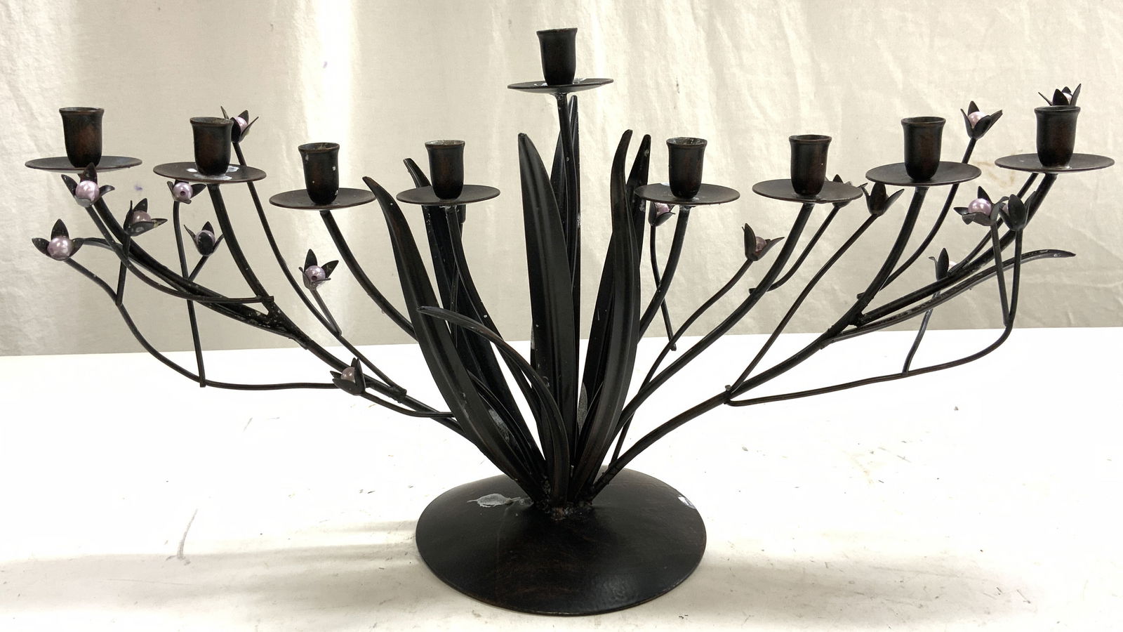 Metal Leaf & Vine Menorah W Beaded Detail: Menorah is bronze toned and metal. Piece has 9 candle areas including center. Piece has floral, vine and leaf structures. Piece has pink toned beaded detail. Base of piece has circular form. Menorah m