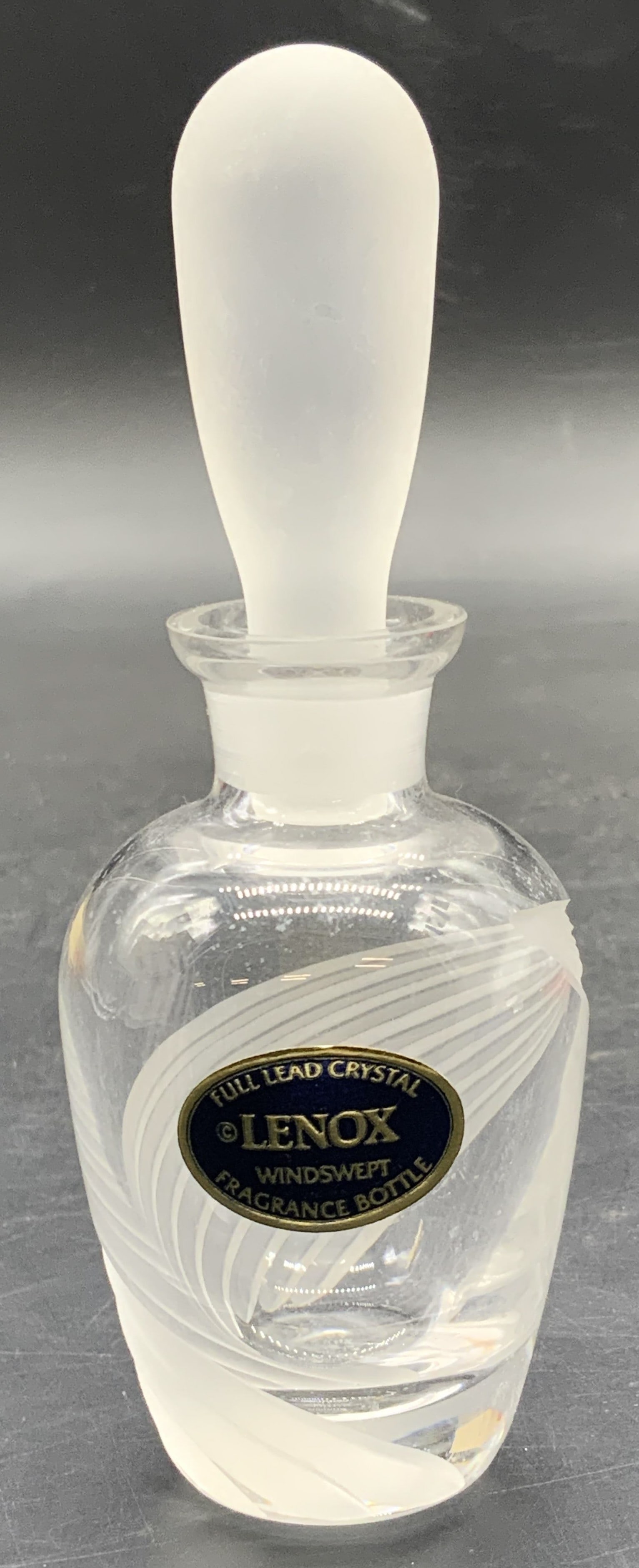 LENOX Full Lead Crystal Windswept Fragrance Bottle: A clear and frosted grooved crystal fragrance bottle. Frosted stopper. Sticker to the obverse reads LENOX Full Lead Crystal Windswept Fragrance Bottle. Underside signed LENOX. Measures approx. 5H x 1.