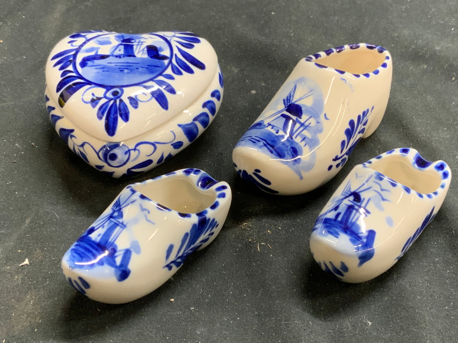 Lot 4 Dutch Porc Clogs & Heart Trinket Box W Lid: Underside of trinket box reads ELESVA HOLLAND, undersides of clogs read HAND PAINTED, 1 clog reads DELFTS AWP. Lot includes 1 trinket box & 3 Porcelain clogs. Trinket box measures approximately 2.75 i