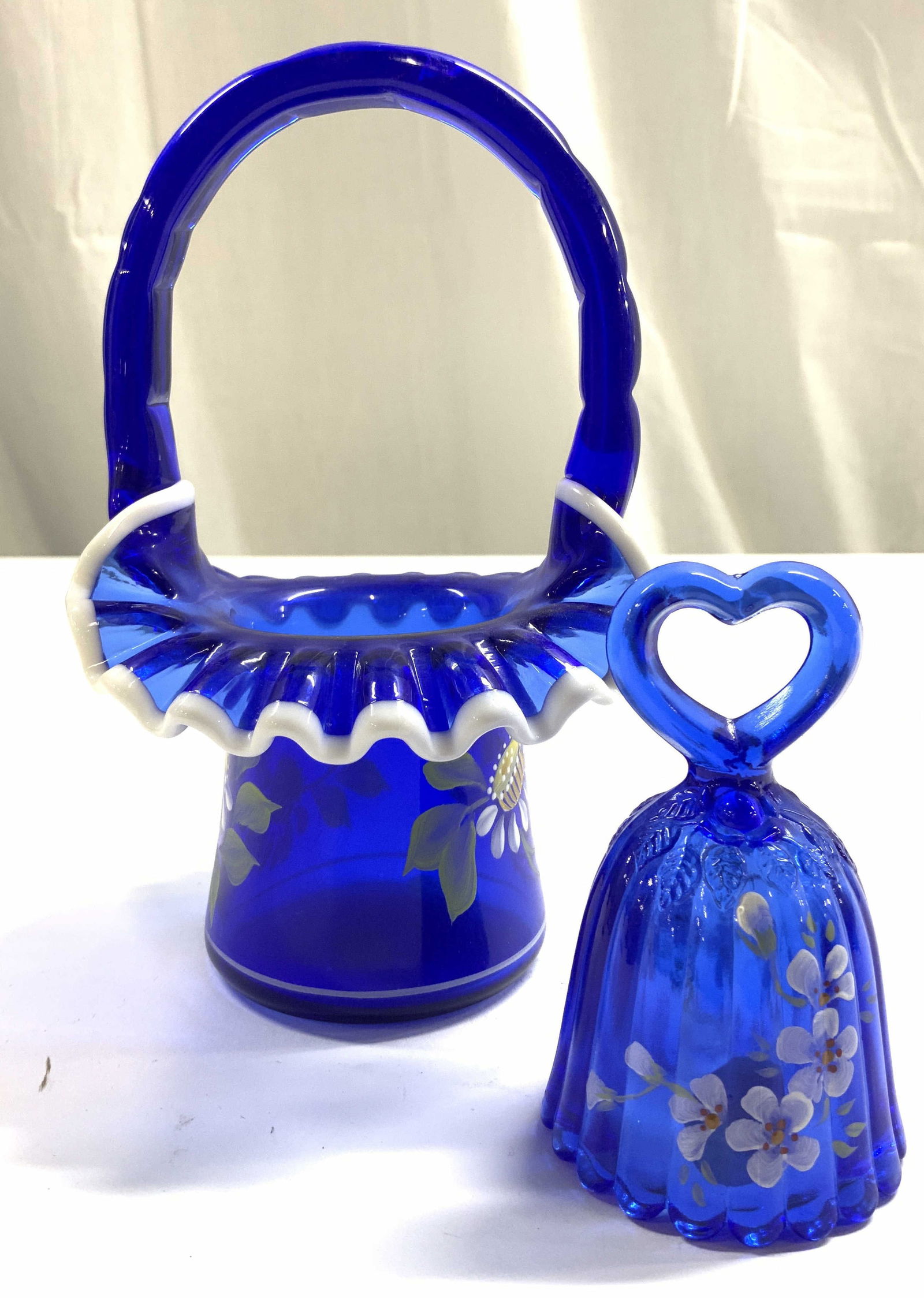 Signed Lot 2 Art Glass Basket & Bell: Each piece reads HAND PAINTED. Each are signed illegibly. Lot includes 1 art glass basket & 1 art glass bell. Each piece is blue toned with multi toned floral and leaf detail. Basket has white toned r