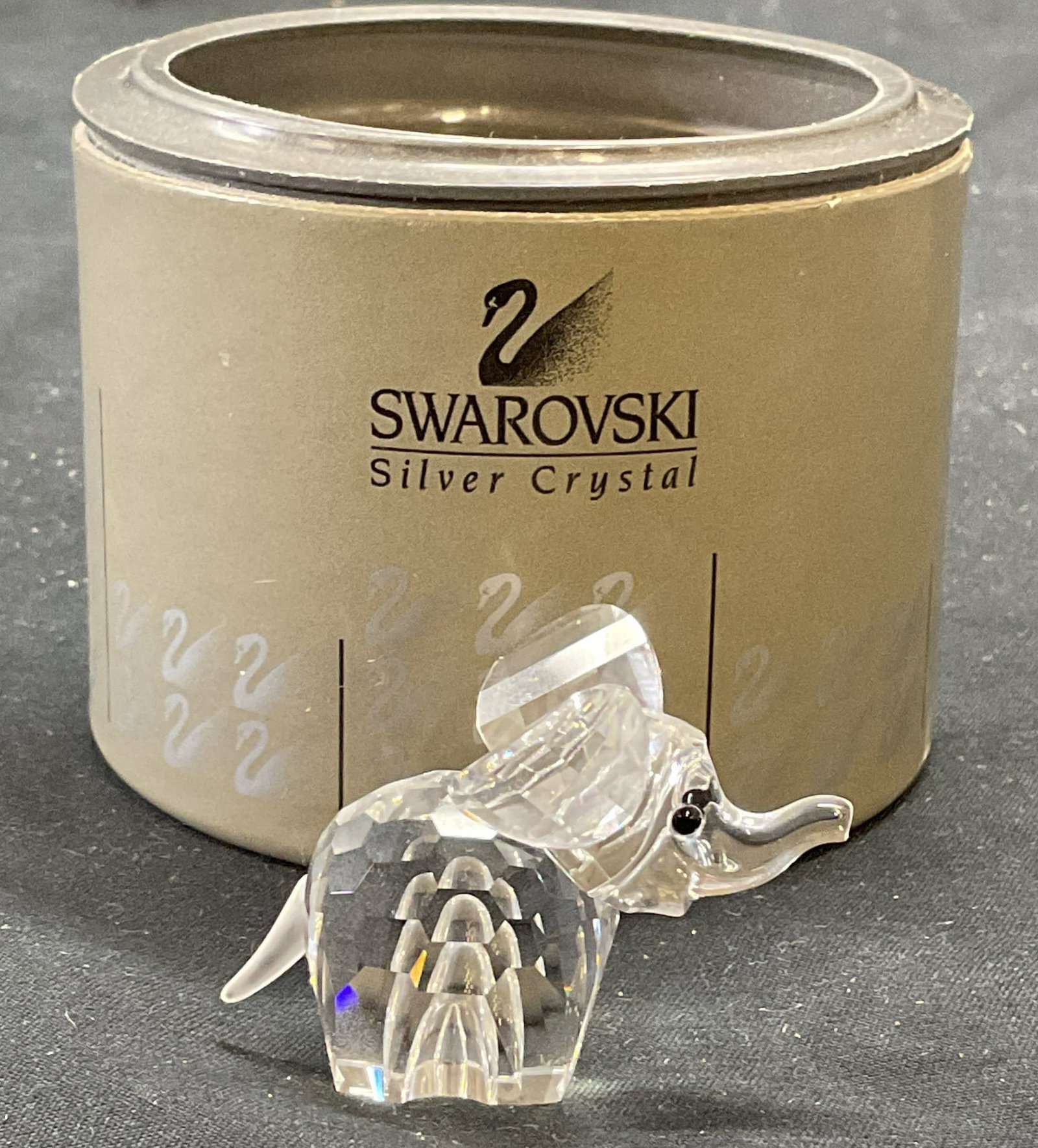 Swarovski Crystal Elephant Figurine with Box: Swarovski crystal elephant figurine. Includes original protective box. Figurine measures approx. 2 x 1.25 x 1 3/8 inches. Signed to underside. Some surface wear consistent with exposure.