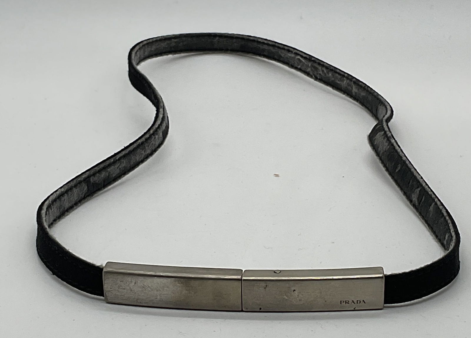 Prada Black & Silver Tone Belt: Prada black fabric and silver tone metal buckle belt. Signed on buckle. Measures approx. 28 inches long. Wear to material including rubbing, scratching, and peeling observed. Prada, Prada belt, ladies