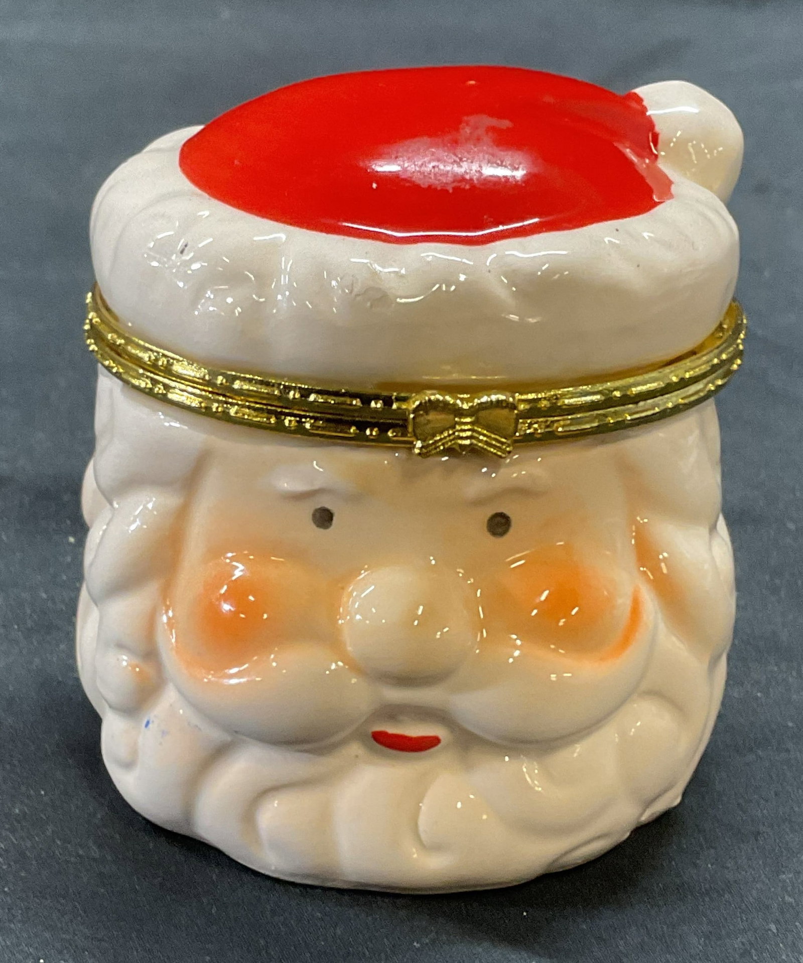 Porcelain Santa Head Trinket Box: Porcelain Santa head trinket box. Hues of red and white. Gold tone rim with bow detail. Measures approx. 2.75 x 2.75 inches. Some surface wear including scratching observed. Santa, Santa trinket box, 