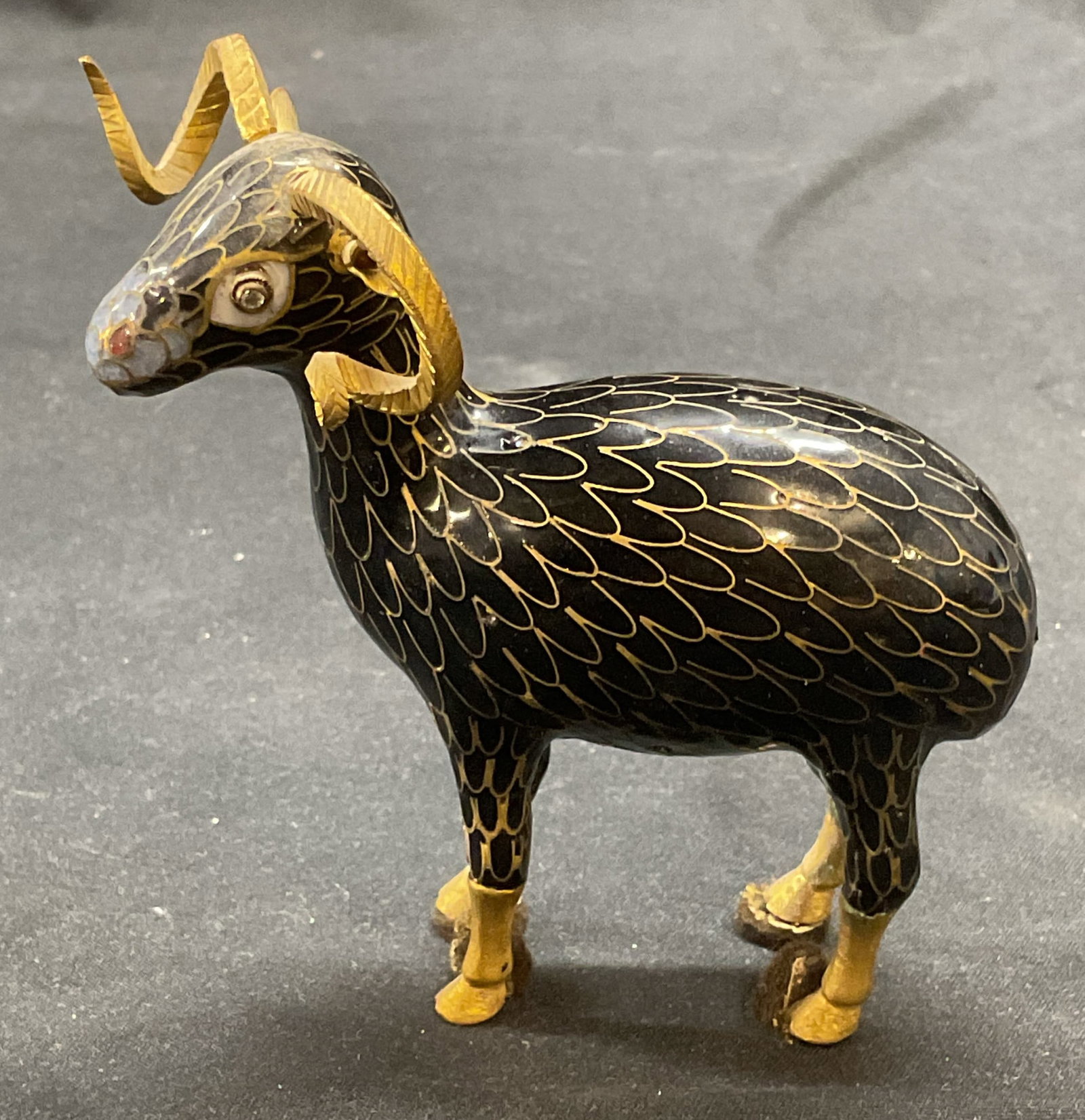 Gilt Black Cloisonne Ram Figural: Cloisonne Ram figural. Black and blue enamel and hand painted gilt decoration over metal. Crystal eye decoration. Measures approx. 3.5 x 1 x 3.75 inches. Some surface wear consistent with exposure. Cl