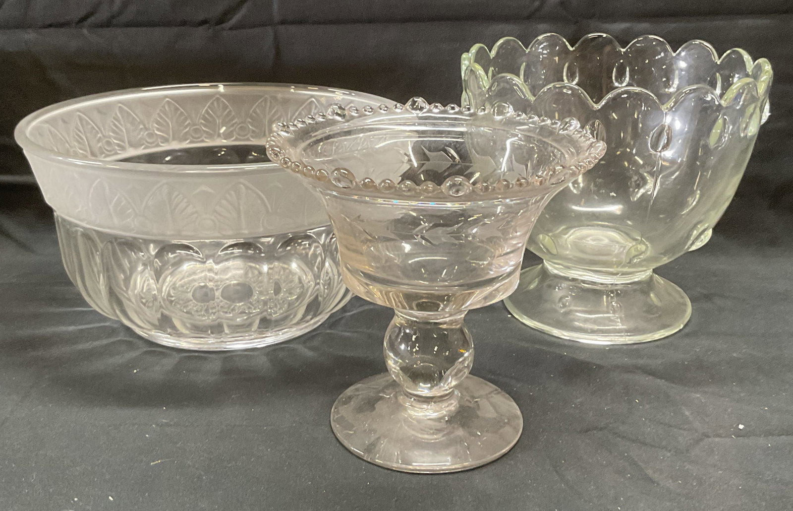 Lot 3 Glass Footed Bowls & Serving Bowl: 2 footed glass bowls with raised bead patterns. 1 glass serving bowl with botanical pattern. Largest bowl measures approx. 10 x 5 inches. All pieces he some surface wear including scratching observed.