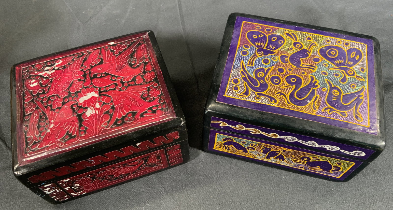 MARIA ROSENDO Hand Crafted Trinket Boxes: Two trinket boxes. One box has a red and black motif with bird and floral engravings. The other has a colorful motif with birds, butterflies, and bunny engravings. Boxes measure approx. 4.25 W x 2.5 H