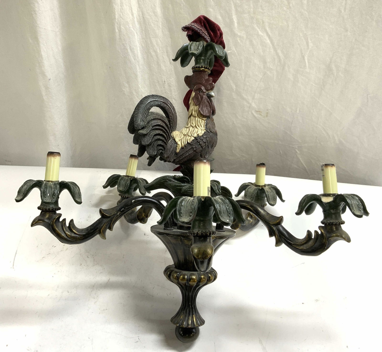 Vntg Composite 5 Arm Rooster Chandelier: Chandelier is vintage. Piece is crafted with a composite material. Piece has 5 arms, each with leaf detail & candlestick style bulb sockets at ends. Top of piece has rooster figure. Chandelier has cha