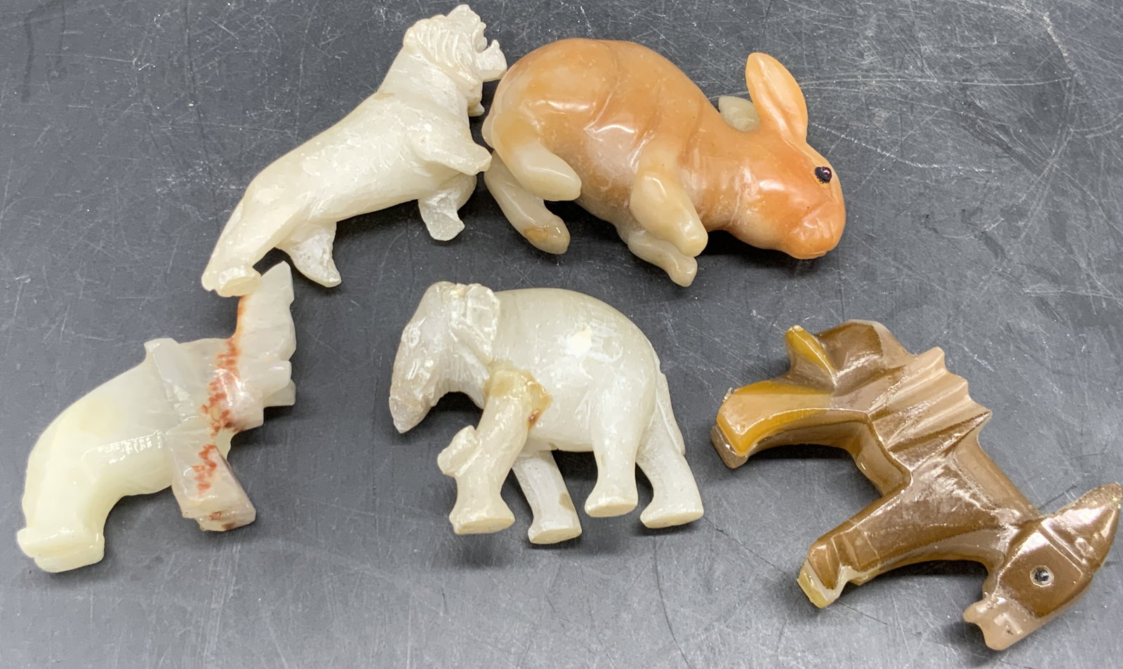Lot 5 Natural Stone Animal Figurals, Rabbit +: Five natural stone animal figurals. Pieces are crafted from stone. Various colors to the pieces. Animals include elephants, a rabbit, a donkey, and a feline. The rabbit has pink costume cabochon eyes.