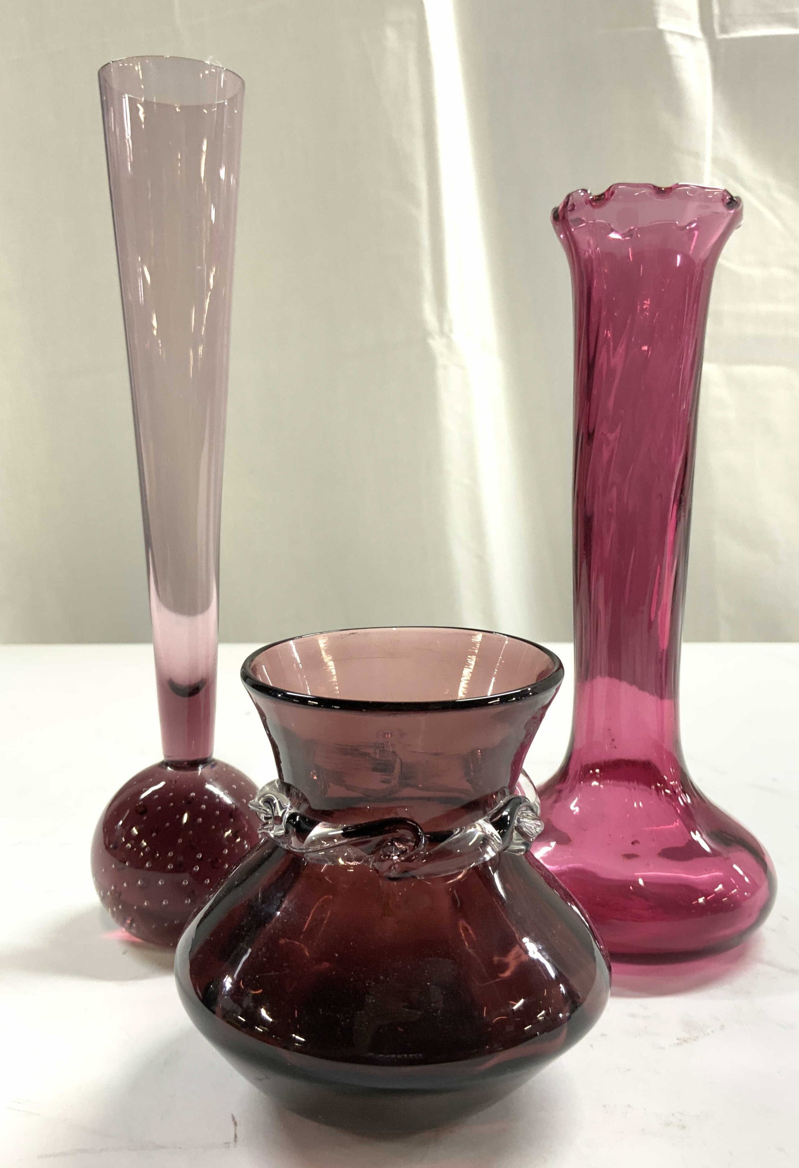 Lot 3 Art Glass Vases Vessels Amethyst / Purple: Lot includes 3 vases. Each have varying amethyst / purple hues. Includes 1 vase with handkerchief style rim, 1 with spherical bubble detail base & 1 short vase with clear detail around neck. Largest v