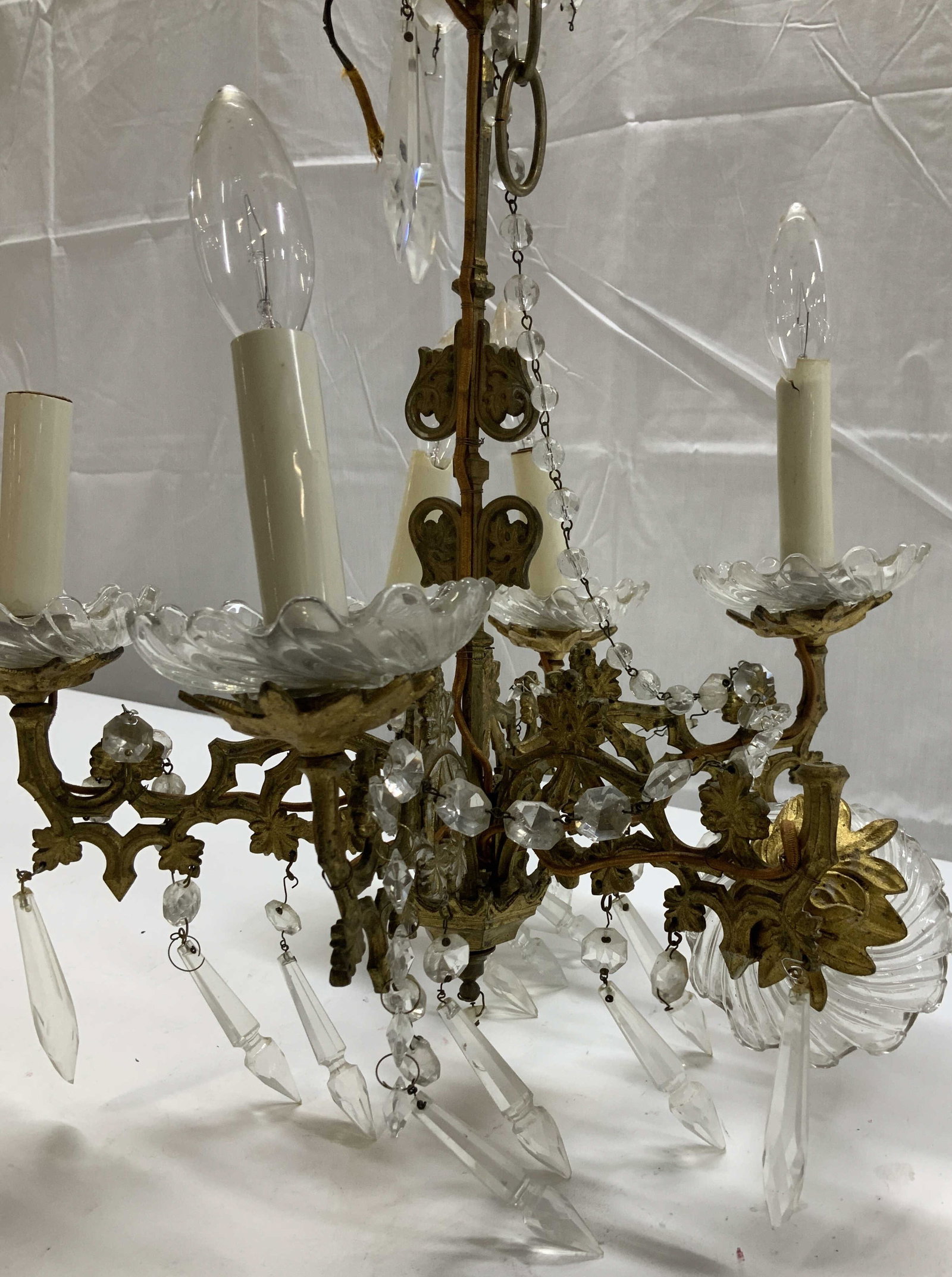 Gilt Brass 6 arm Ornate Vntg Chandelier w Prisms: Gilt brass chandelier with 6 arms, glass bobeches, and dangling prisms. Overall wear. Not tested for working condition. Needs repair . One light socket is off of arm. Worn gilt. Measures 15.5 in. Long