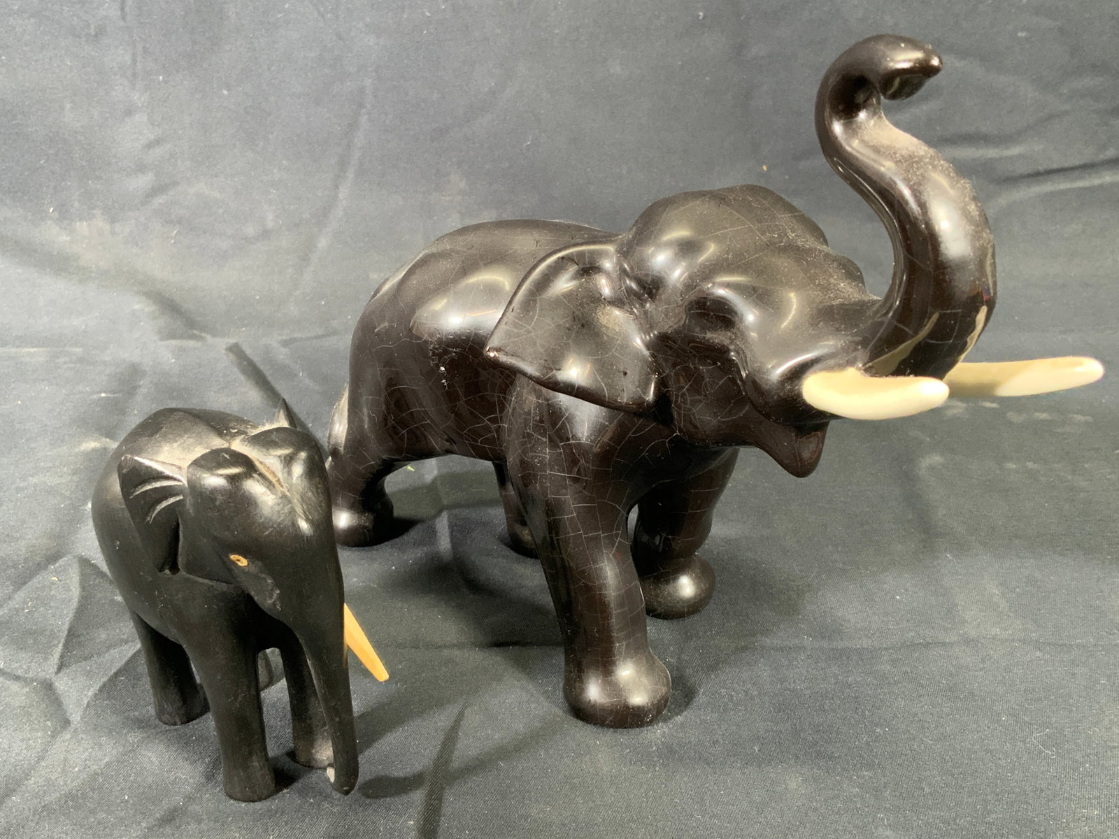 2 Lot Black Wooden & Ceramic Elephants: Two black elephants. Larger elephant is ceramic. Measures approx. 8 W x 6.5 H x 3 D. Crazing to ceramic. Smaller elephant is wooden. Loss of one tusk. Decorative arts, home decor, tabletop accessories