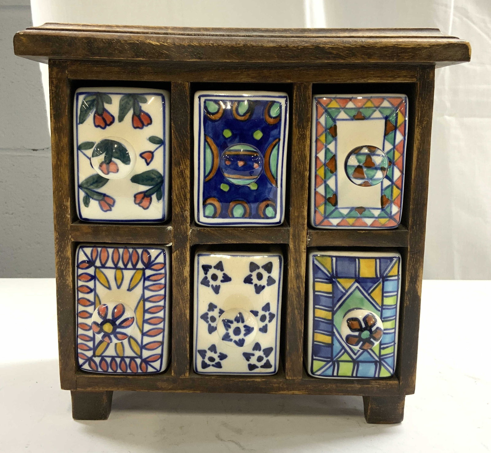 6 Drawer Wood & Porcelain Chest: Chest has brown toned wooden frame. Piece has 6 porcelain drawers with geometric patterns & floral detail. Each drawer has knob form handles. Piece measures approximately 9.75 inches wide 9.5 inches t