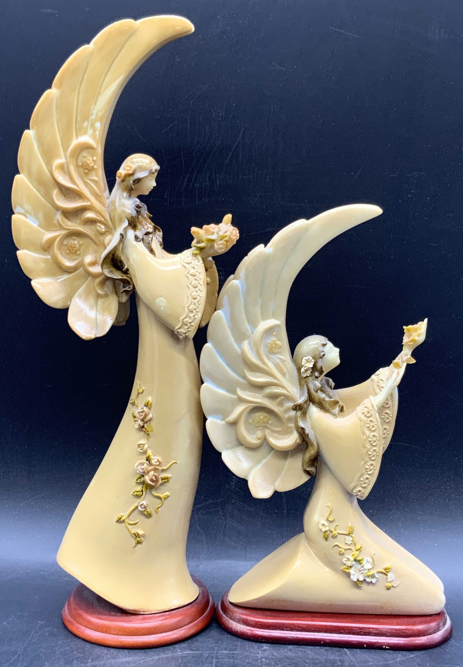 2 Standing & Kneeling Resinous Angel Figurals: Two resinous angel figurals. The two angels are attached to wooden bases and depicted either standing or kneeling. Raised floral motif to the angels. Taller piece measures approx. 12.5H x 4.25W in. St