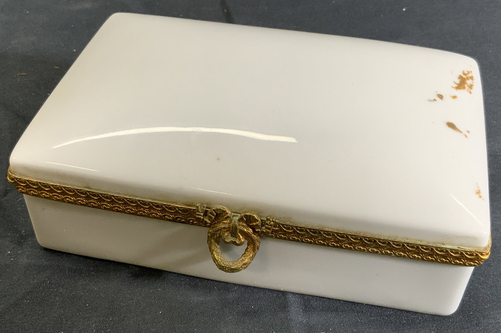 LIMOGE Porcelain Hinge Box, France: Porcelain box. Gold toned metal trim on inside borders with scrolling motif. Gold toned wreath clasp. Underside reads Limoges France. Box measures approx. 5.5 W x 1.5 H x 3.5 D in. Box has residue on 
