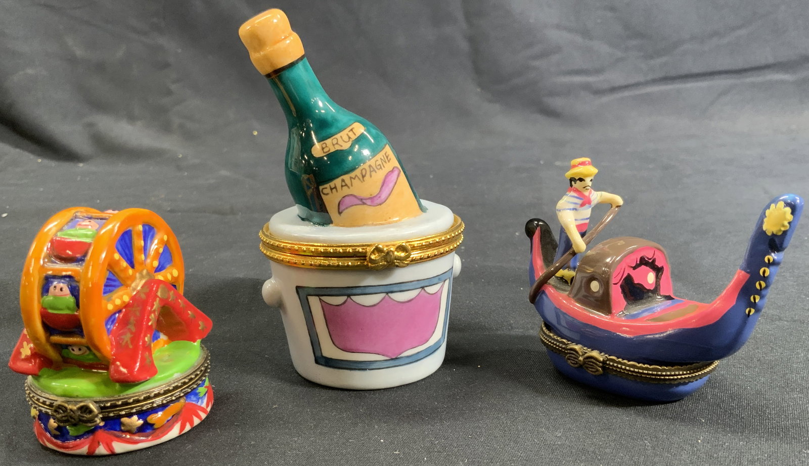 Porcelain Hinged Themed Trinket Pill Boxes: Three porcelain hinged trinket pill boxes. Champagne Brut wine bucket figural. Hand painted and lettered. Gold toned metal rim and hinge with bow motif clasp. Measures approx. 2.25 D x 4 H in. Ferris 