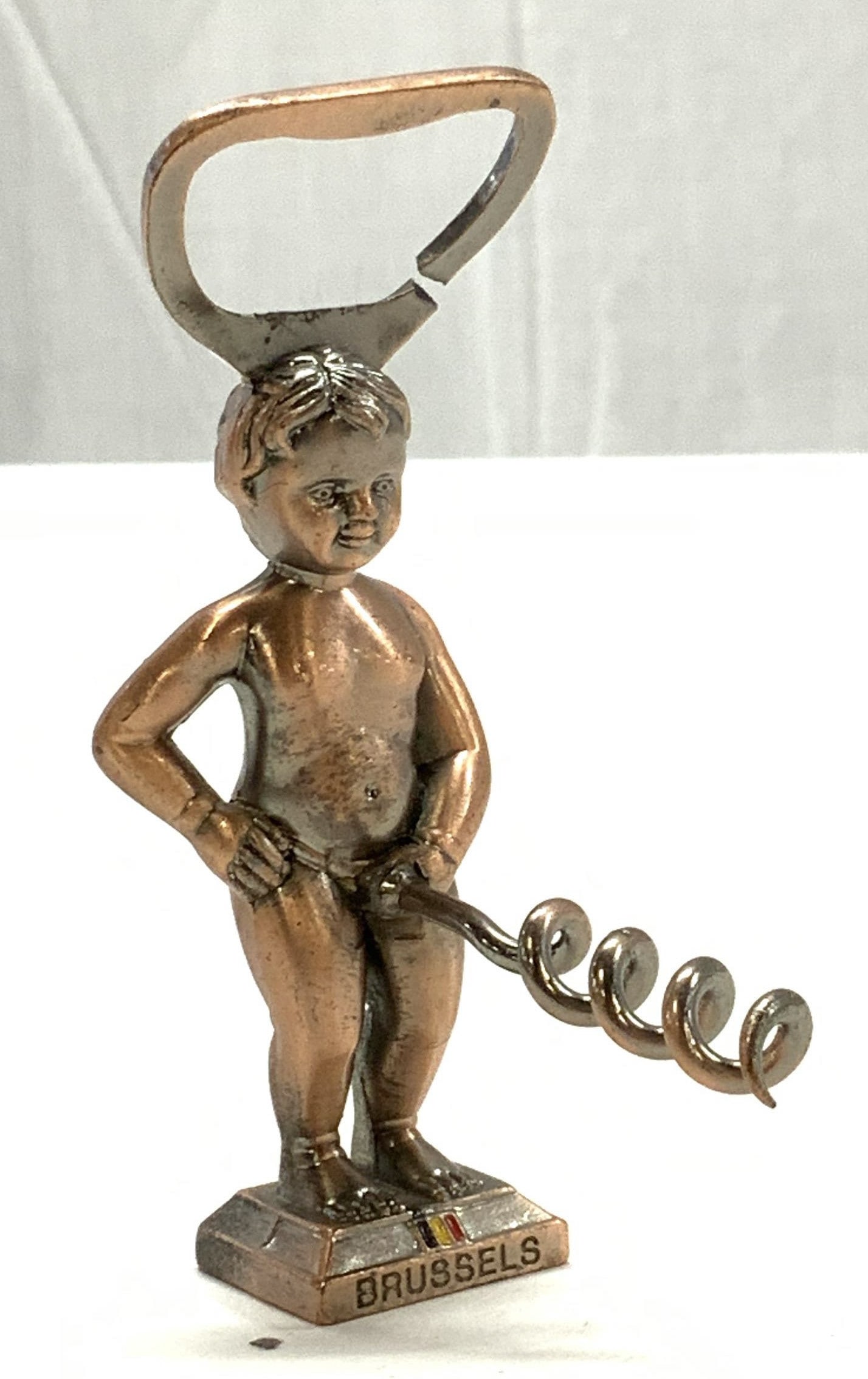 Copper Plated Metal Bottle Cap Opener, Brussels: Figural bottle cap opener, copper patina over base metal. Separated bottle cap opener. Has a cork screw. Items reads Brussels. Measures 3.7/8 in. Tall / long x 1.25 in. Wide. Brussels souvenir, bottle