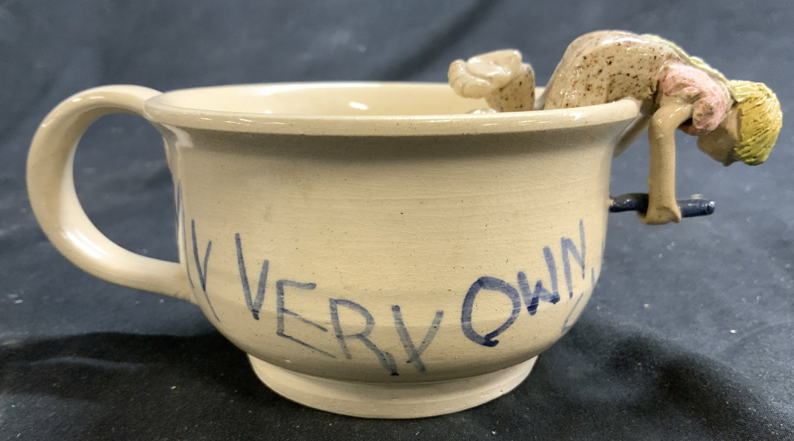 Signed Ceramic Teacup W Figural: Underside is signed Illegibly (first name appears to read JILL). Teacup is vintage and ceramic. Piece has barefoot figure hanging on side of piece writing MY VERY OWN CUP. Cup measures approximately 6