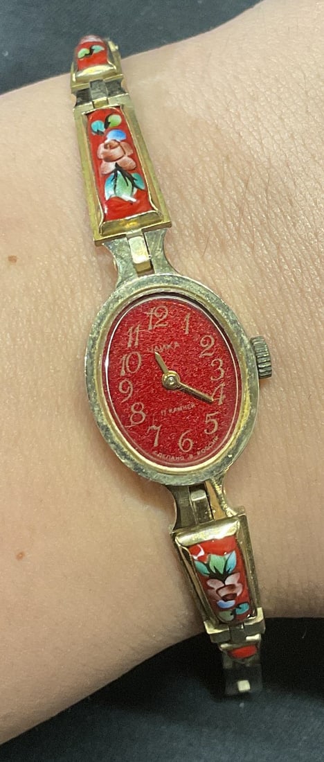 Vintage Hanka Russian Gold Tone Watch: Vintage hanka Russian gold tone watch with red face and enameled floral decoration on band. Signed on face. Measures approx. 7 inches long. Not tested for function. Some surface wear including scratch