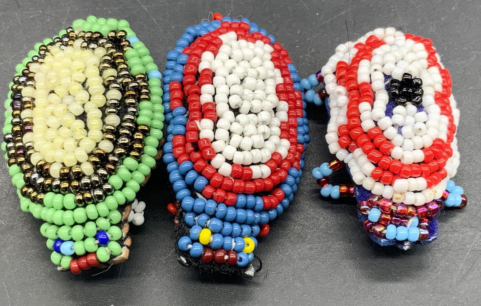 Lot 3 Multicolored Seed Beaded Animal Pins: Three multicolored seed beaded animal pins. Crafted from leather and beads. Metal safety pins to the undersides. Largest beetle measures approx. 1.75L x 1.25W in. Some surface wear and loose threads p