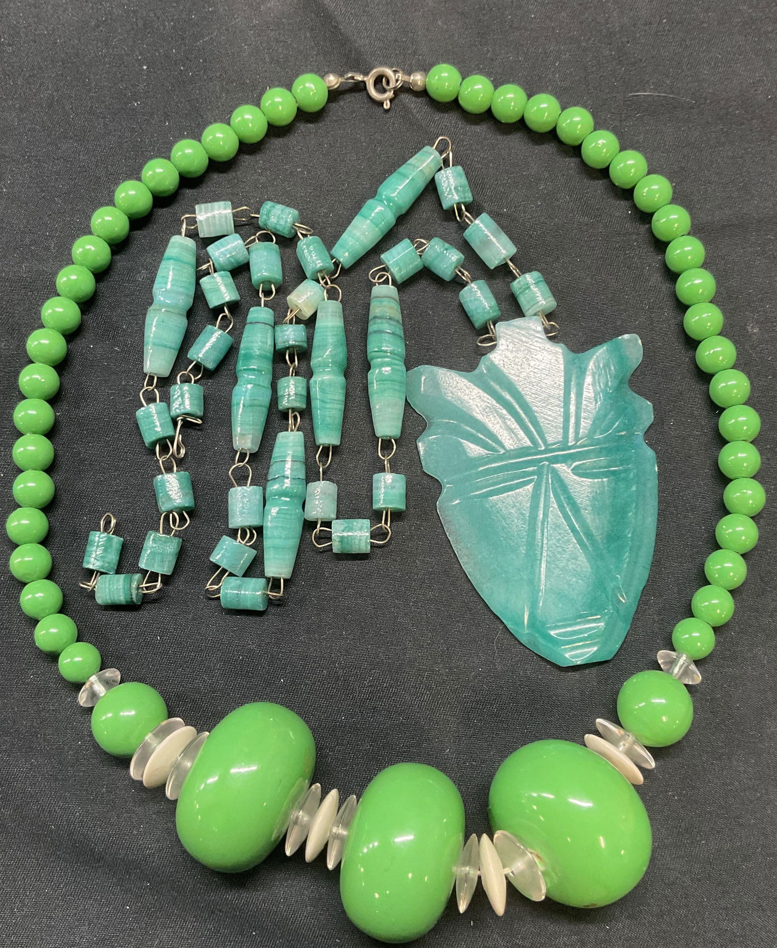 Lot 2 Carved Blue Stone Pendant Necklace +: Carved blue stone pendant necklace. Drop length approx. 12 inches. Pendant measures approx. 3 x 2 inches. Green, white, and clear beaded choker necklace. Drop length approx. 8.5 inches. Some surface w