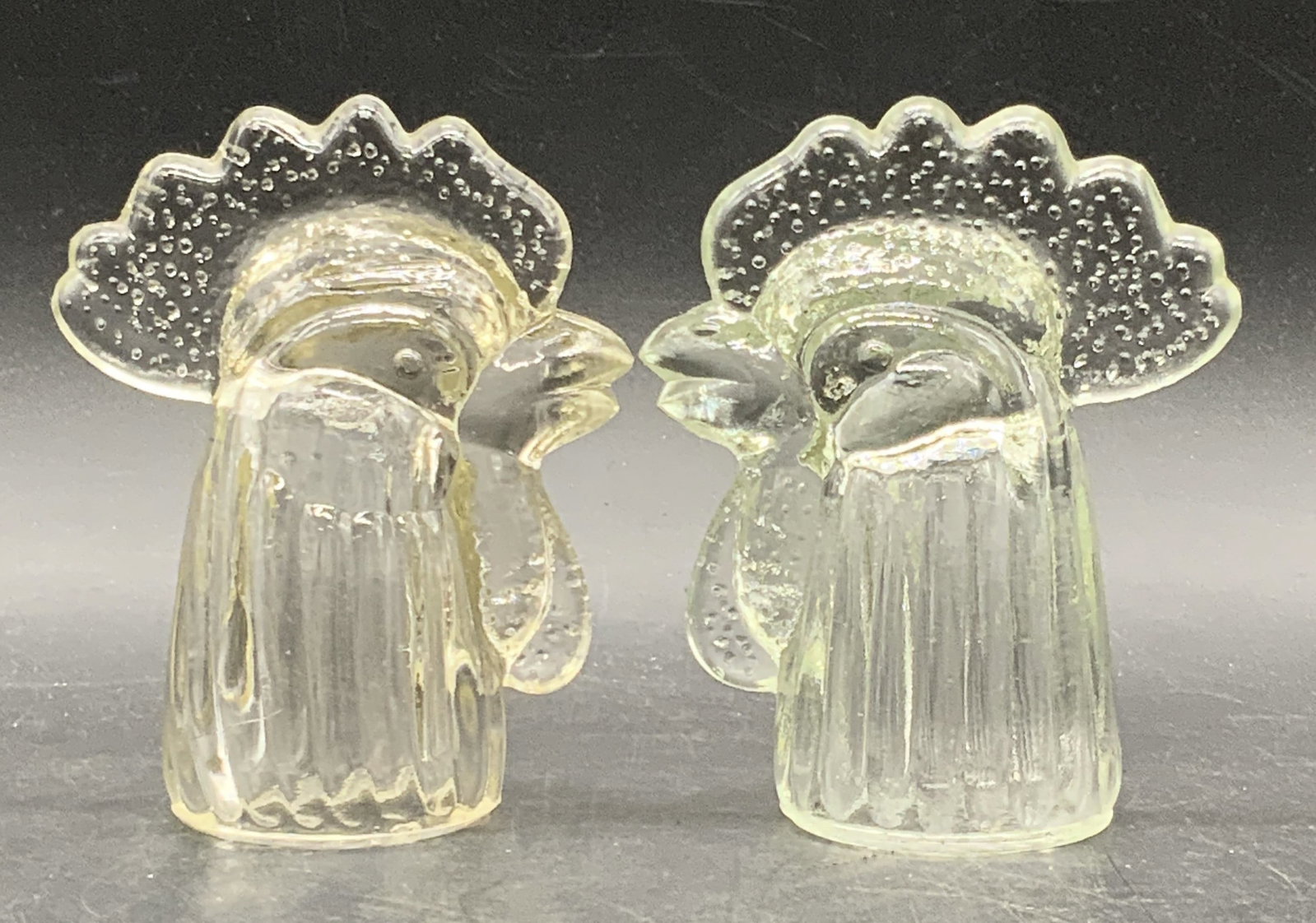 Pair Vintage Clear Glass Rooster Head Figurals: A pair of vintage clear glass rooster head figurals. Light hue to both pieces. Measures approx. 4.5H x 3.5W in. Seam present to glass. Some wear consistent with age, use, and exposure. Cracking / impe
