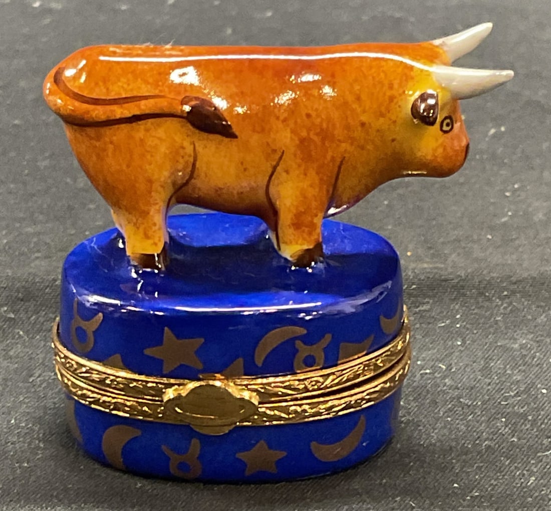 Limoges Artoria Porcelain Taurus Trinket Box: Limoges Artoria hand painted porcelain trinket box. Taurus zodiac symbol motif. Gold tone rim with planet detail. Trademarked to underside. Signed SB, numbered 58. Made in France. Measures approx. 2 x