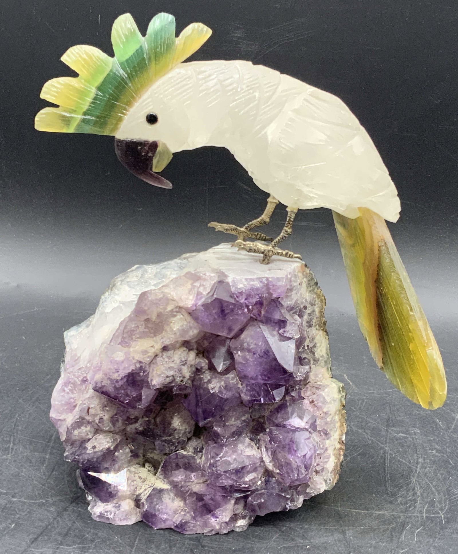 Carved & Etched Natural Stone Cockatoo on Amethyst: A carved and etched natural stone cockatoo figural atop an amethyst specimen. Two drilled holes to the top of the amethyst for the metal feet of the cockatoo to rest in. Together pieces measure approx