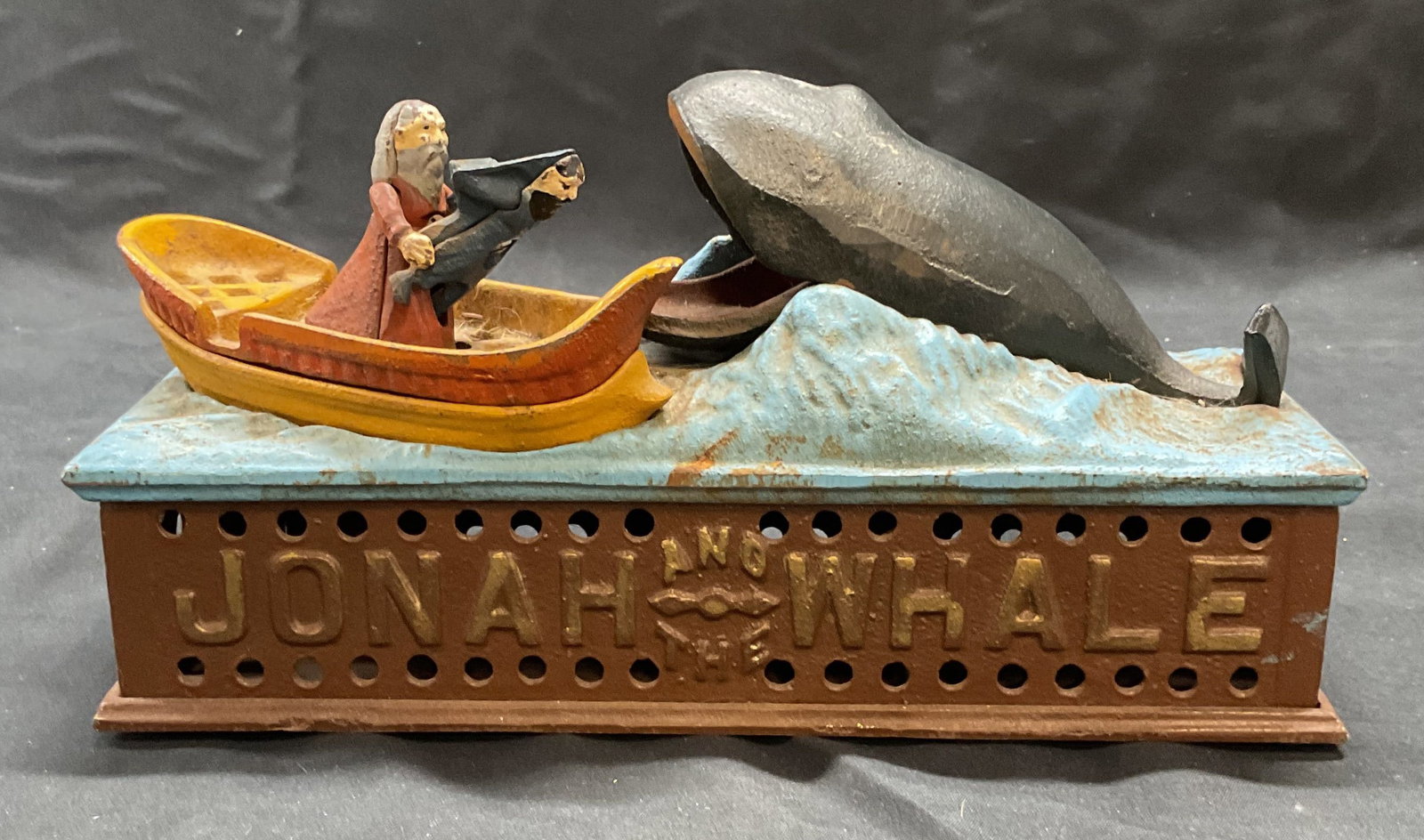 Jonah & The Whale Mechanical Iron Coin Bank: Antique reproduction Jonah and the Whale cast iron coin bank. Painted in hues of blue, yellow, and red. Lever on side moves figures to deposit coins in whale mouth. Marked on underside Reproduced from