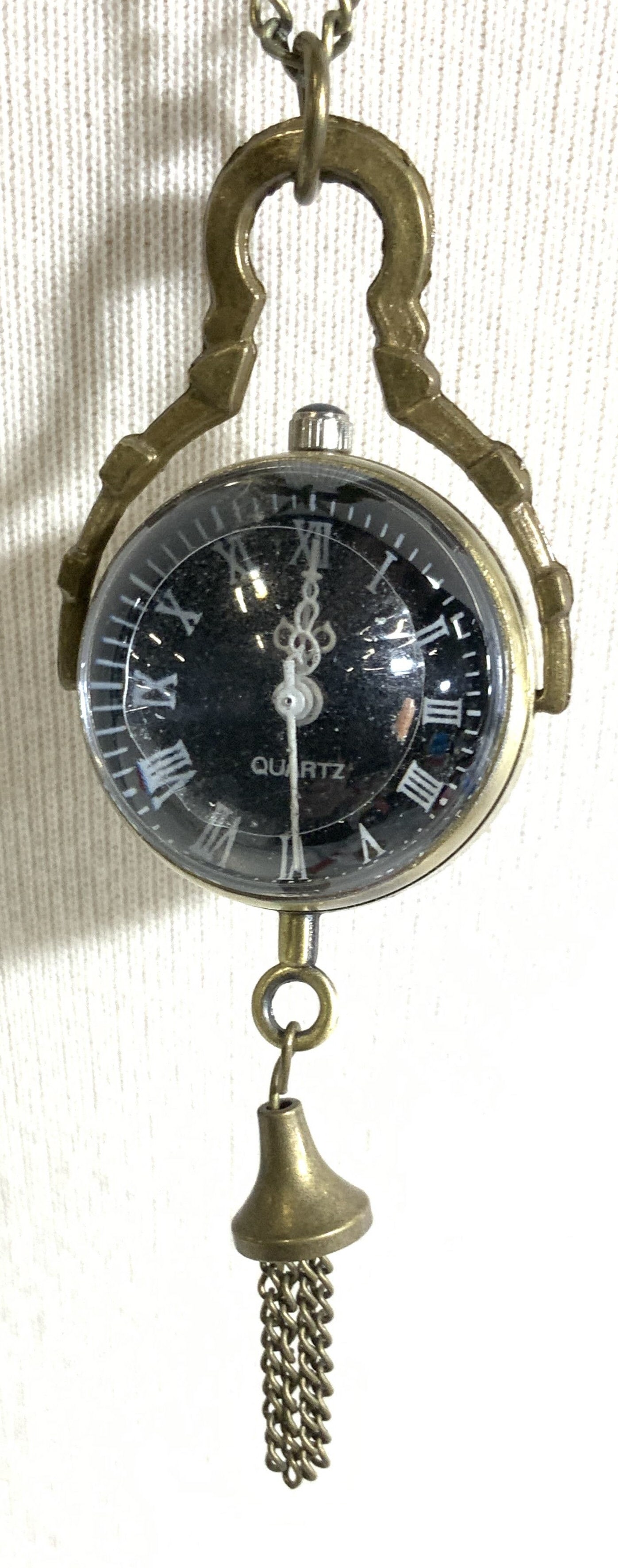 Victorian Trading Co Quartz Pendant Watch Necklace: Long chain necklace with 13 in. Drop that has a concave Quartz clock pendant with a bell tassel. Battery operated, backside reads 897S, battery 377S comsan Japan ( or equivalent) . Pendant measures 2.