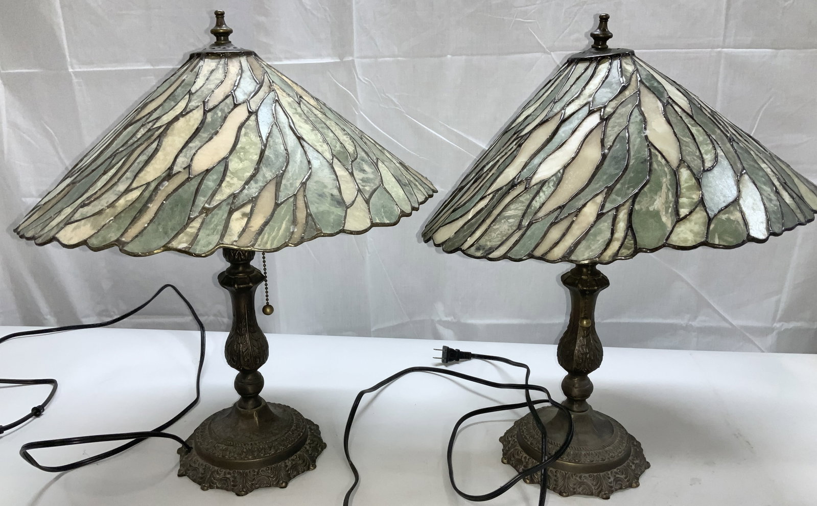 Pair Slag Glass Arts and Crafts Lamps: Slag glass lamps with army green slag glass mosaics. Singular bulb with a pull chain. Heavy metal lamp body. Embossed scroll decor on metal. One lamp has a dent on lamp where the finial is. Lamps meas