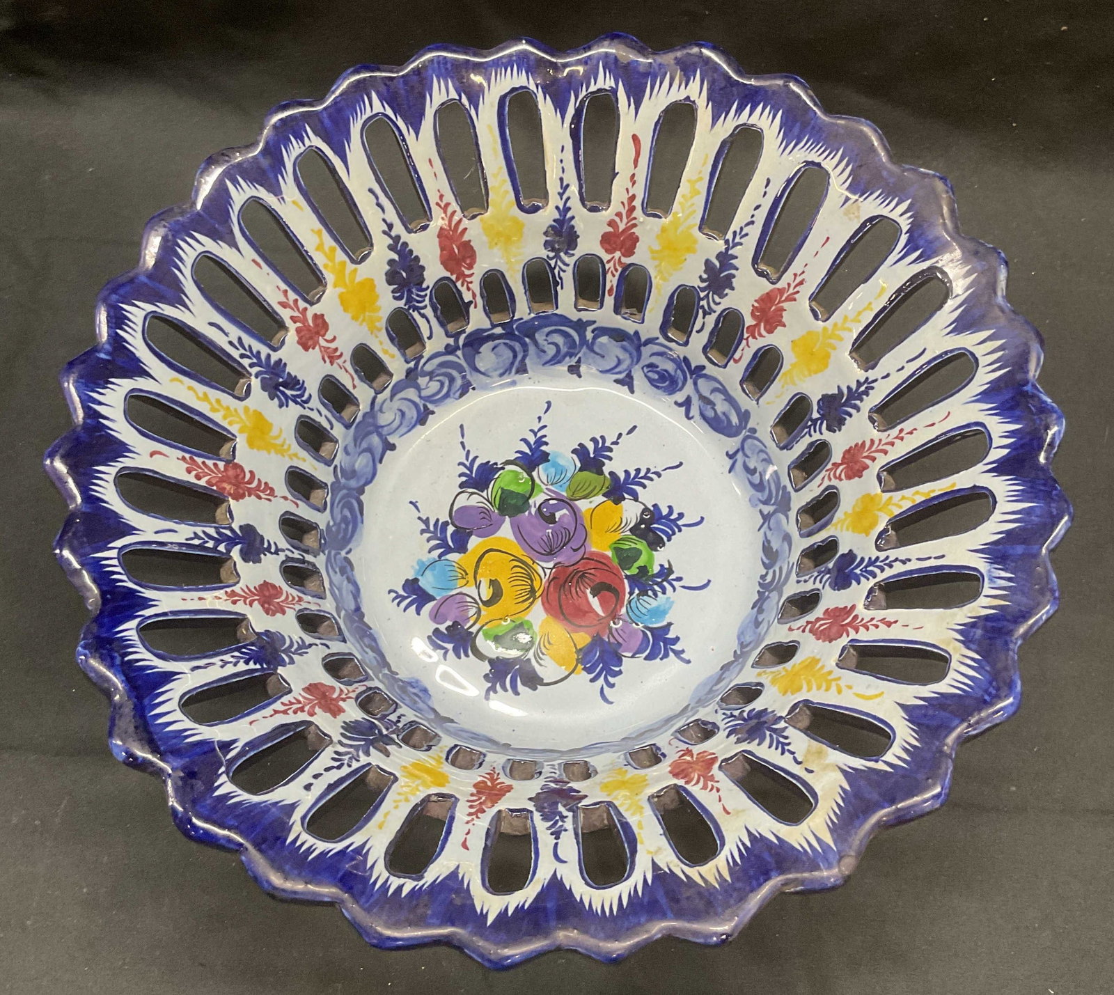 Signed Pierced Porcelain Floral Basket, Portugal: Signed porcelain basket with pierced detail and hand painted decoration. Hues of blue, red, and yellow with floral motif. Signed to underside, illegible. Made in Portugal. Measures approx. 10 x 5 inch