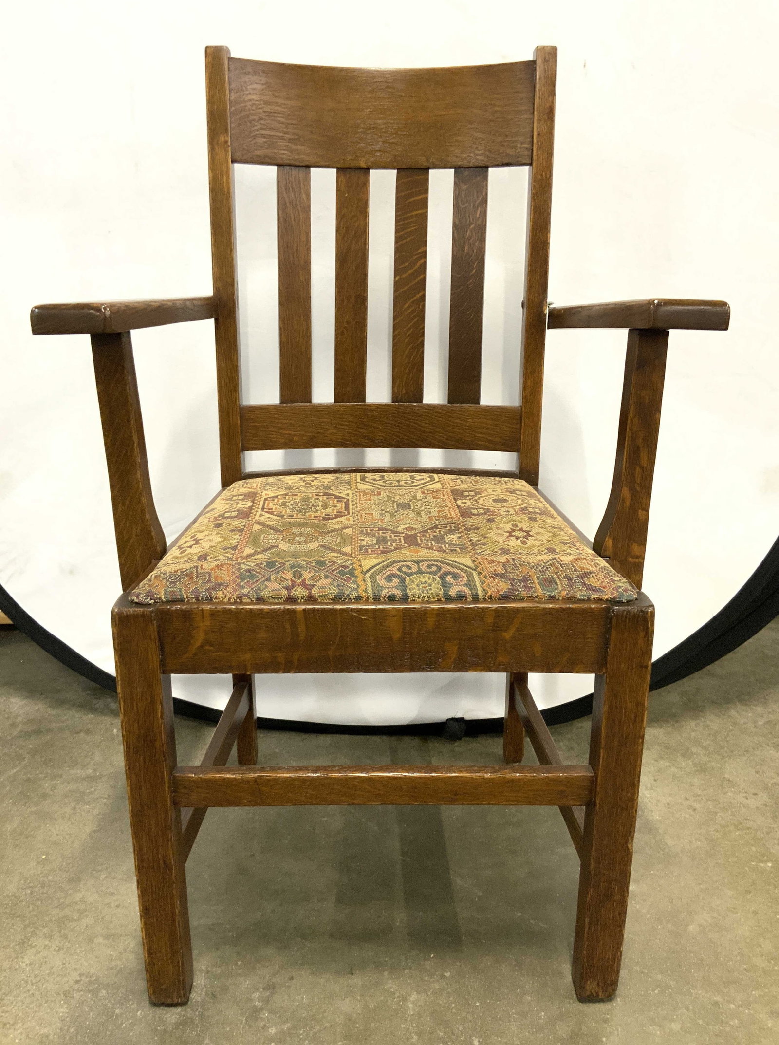 Antique Oak Desk Chair w Uph Seat: Desk Chair appears to be antique possibly vintage. Chair is brown toned and wooden. Piece has intricate multi toned geometric detail. Chair has arms. Piece has 4 legs with box stretcher in between. Ch