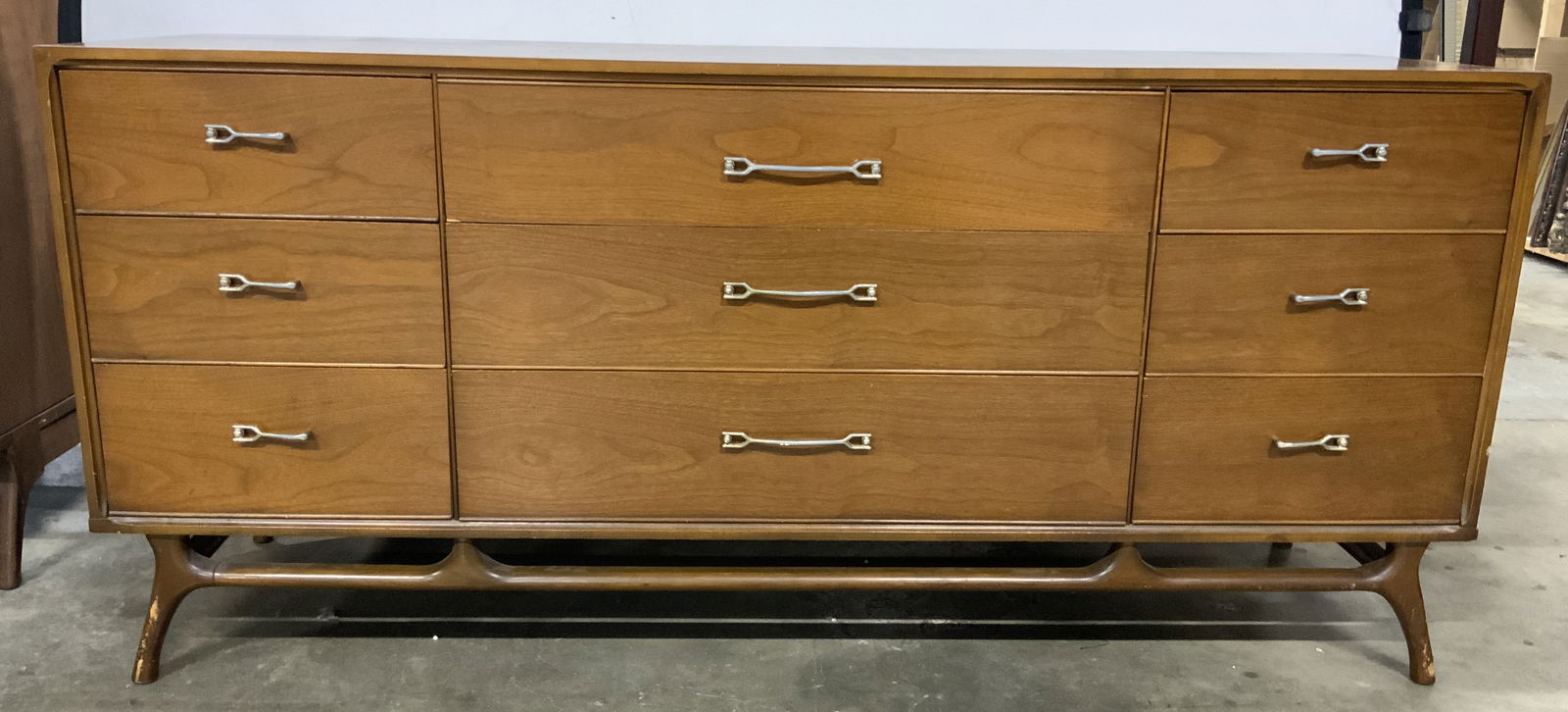 MCM Wooden 9 Drawer Lowboy Dresser: Dresser is mid century modern. Piece is beige toned and wooden. Dresser has 9 drawers each with silver toned metal drawer pulls and dovetailing. Dresser has carved wooden splayed leg support. Measures