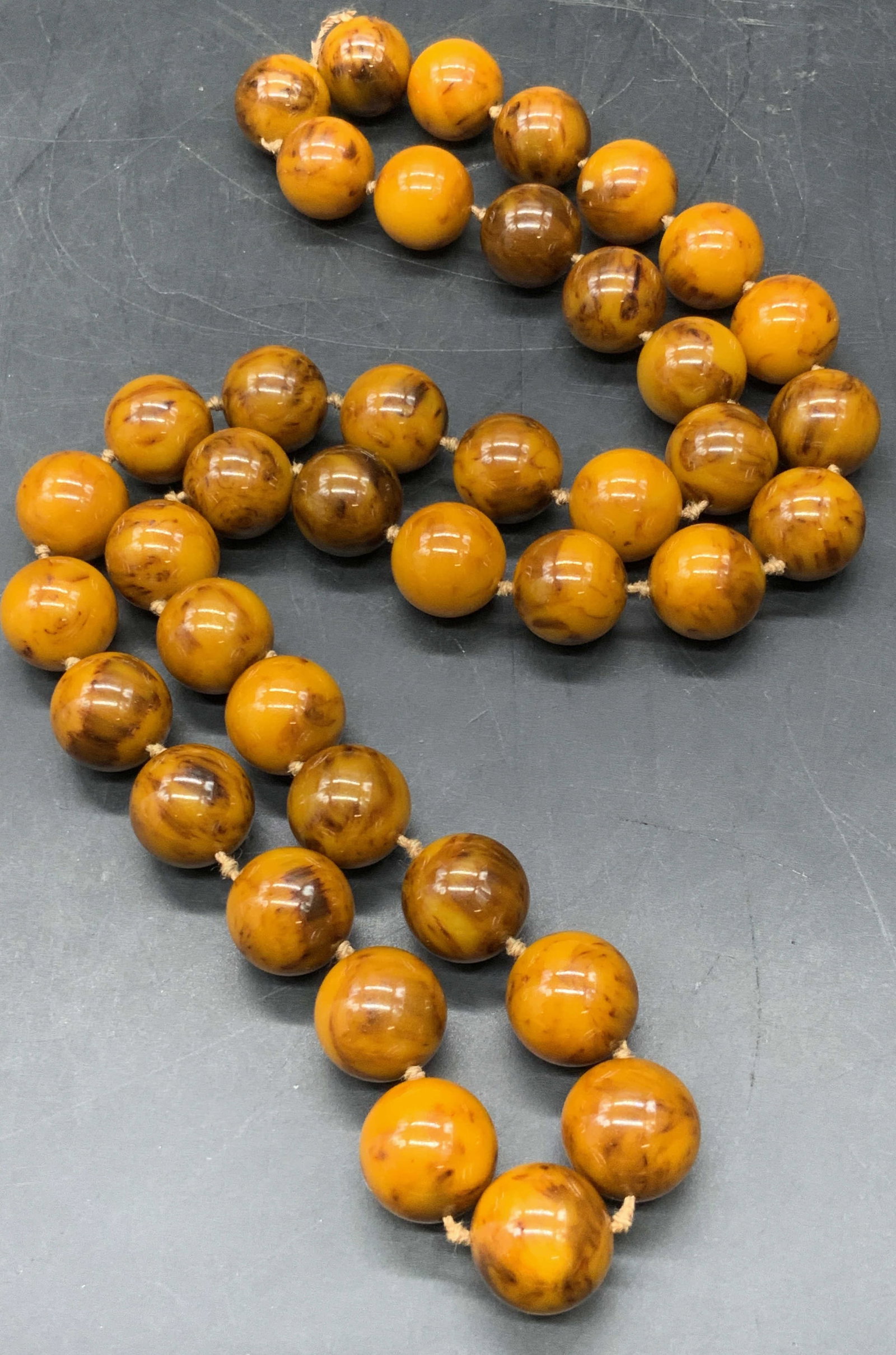 Vintage Amber Beaded Necklace, Jewelry: A vintage necklace comprised of polished amber spheres. Marbled light and dark amber hues throughout. Double knotted. Drop length measures approx. 13.5 inches. Some losses to the string, some surface 