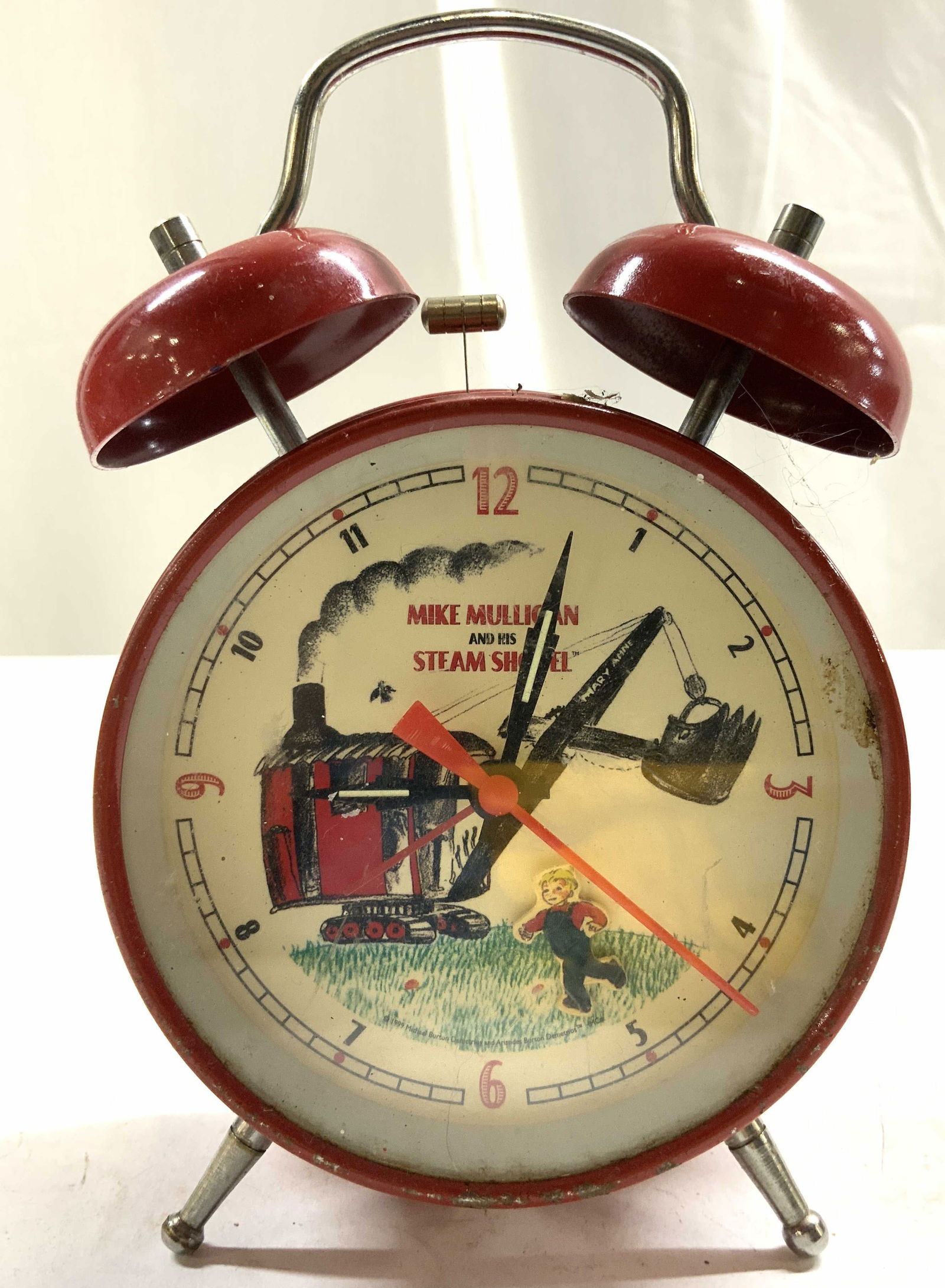 Vntg MIKE MULLIGAN & STEAM SHOVEL Bell Alarm Clock: Clock face reads MIKE MULLIGAN & HIS STEAM SHOVEL. Alarm clock is red toned and metal. Clock face has image of male child figure and steam shovel. Bell alarm clock measures approximately 6.25 inches t