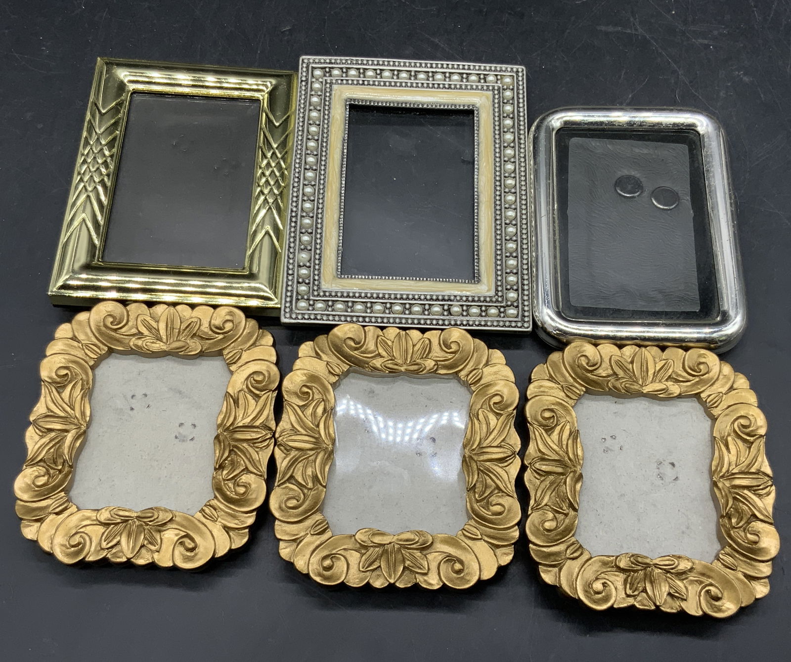 Lot 6 Silver & Gold Toned Picture Frames: Six silver and gold toned picture frames. Five of the six pieces have kickback stands. Pieces are crafted from composite and metal materials. Largest measures approx. 4.25L x 3.25W in. Some surface we
