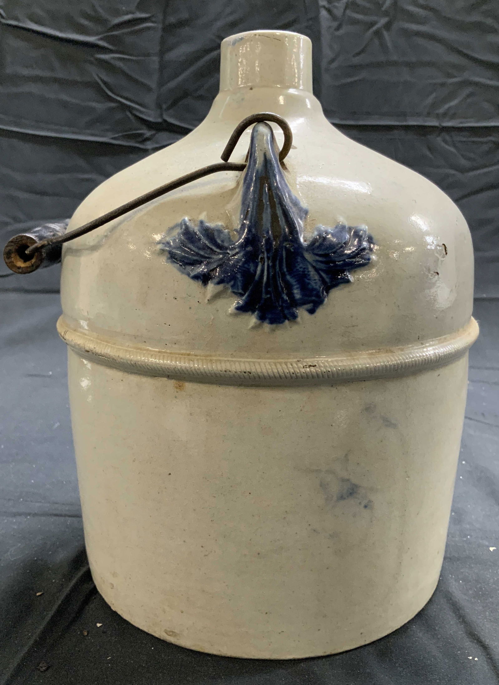 Vintage Stoneware Gallon Jug W Handle: Jug is vintage. Piece is light slate with blue toned areas at sides. Jug is stoneware. Piece has metal and wood handle. Jug measures approximately 10 inches tall 7 inches wide. Jug, gallon jug, stonew