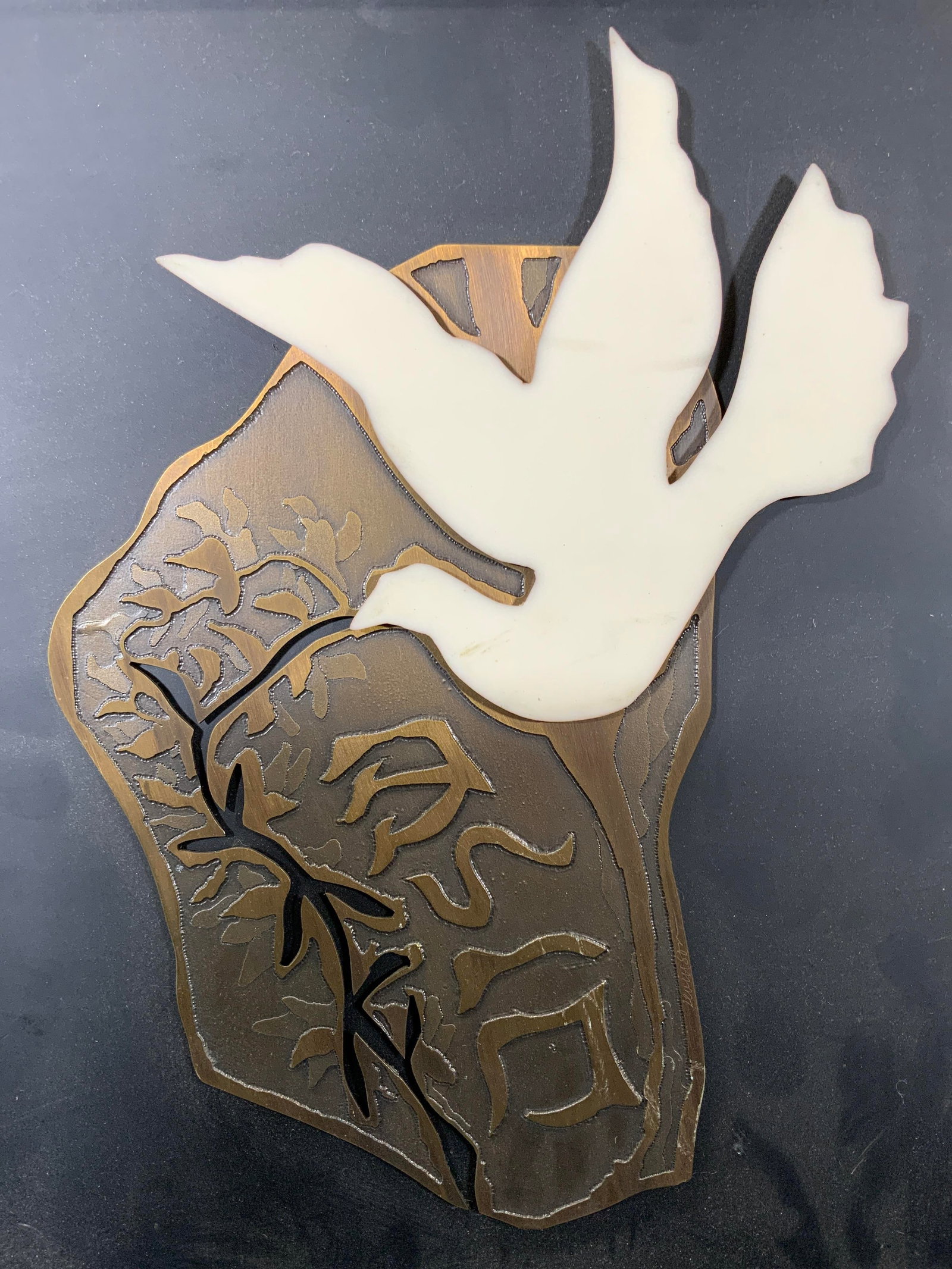 Framed Dove & Olive Branch Wall Hanging: Acrylic and composite motif. Subject depicts a white dove on a copper colored motif with a negative space carved olive branch. Framed in silver toned metal frame, frame measures approx. 12 W x 14 H in