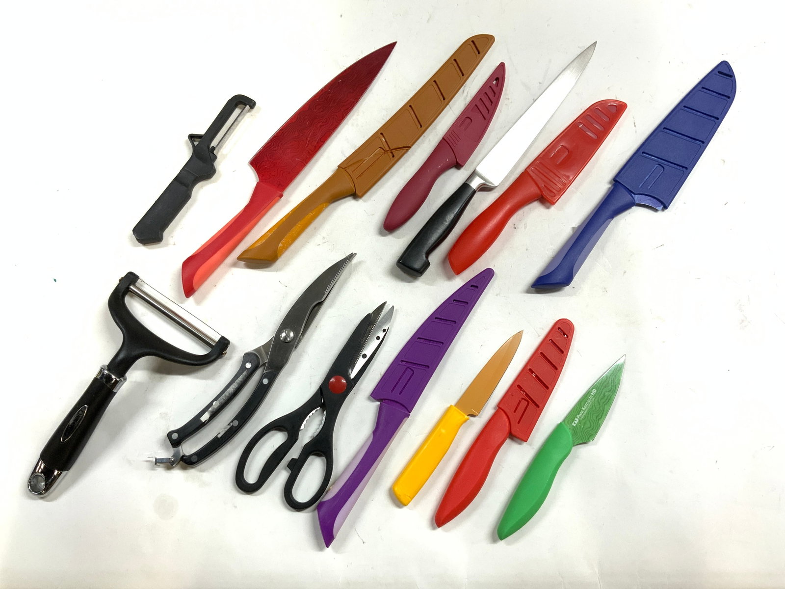 Lot 14 Kitchen Knives, Peelers & Shears: Lot includes 2 peelers, 2 pairs of shears. & 10 kitchen knives. Six knives include knife covers. Lot includes knives in various tones. Largest knife measures approximately 14 inches long. Kitchenware,