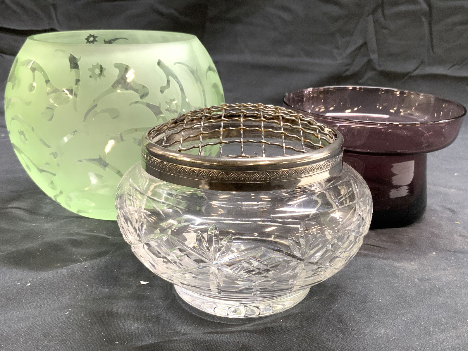 Lot 3 Art Glass Vessels Glass Tabletop: Lot includes 1 purple toned vessel, 1 light green toned vessel with clear detail & 1 vessel with silver toned metal lid. Each piece is glass. Largest piece measures approx 6 inches wide, 5 inches tall
