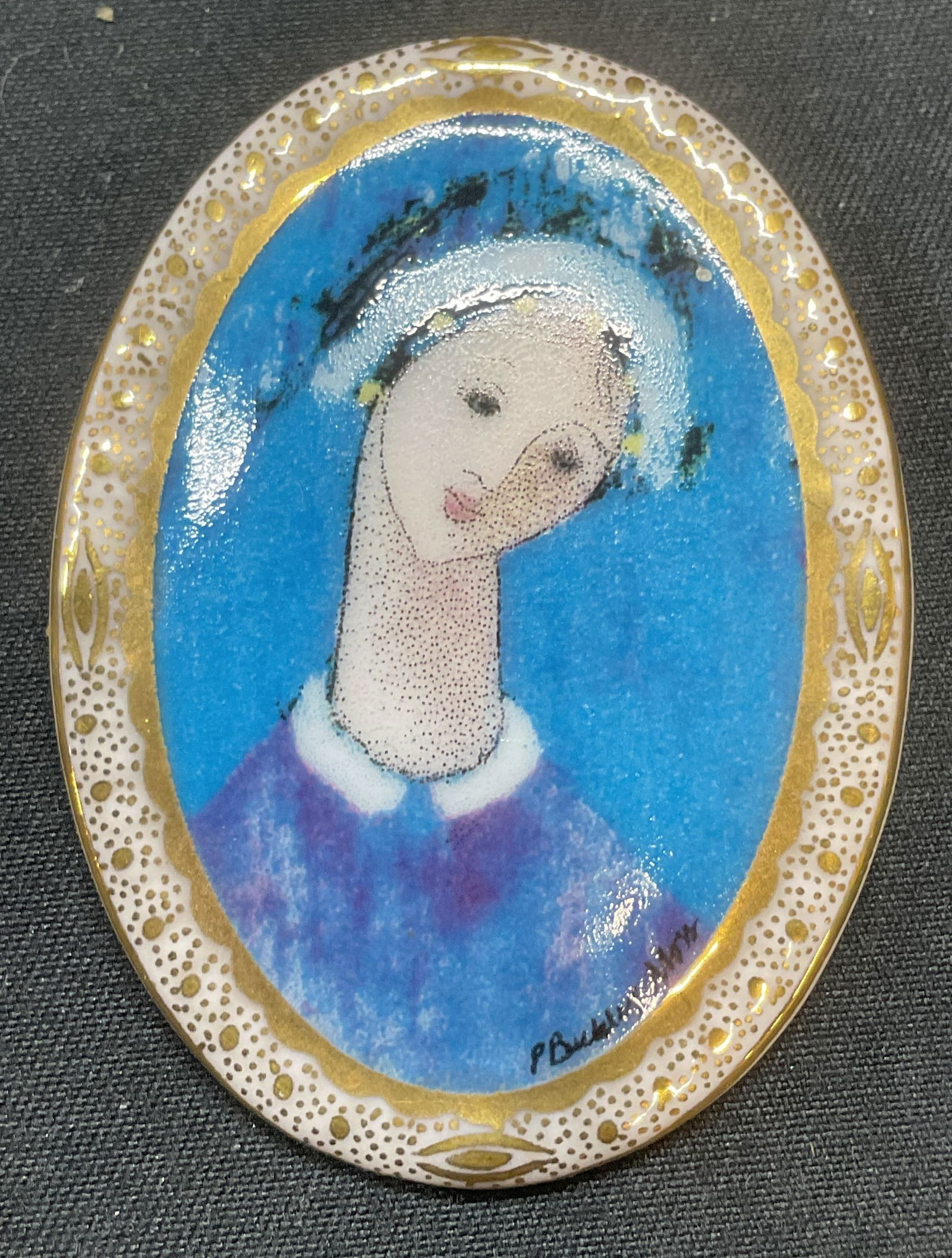 Anna Perenna Blue Madonna Porc Brooch: Vintage 1997 Anna Perenna Blue Madonna porcelain brooch. Madonna motif with gilt decoration. Signed to underside. Artwork by Patricia Buckley Moss. Hinge pin to underside. Measures approx. 2 x 1.5 inc